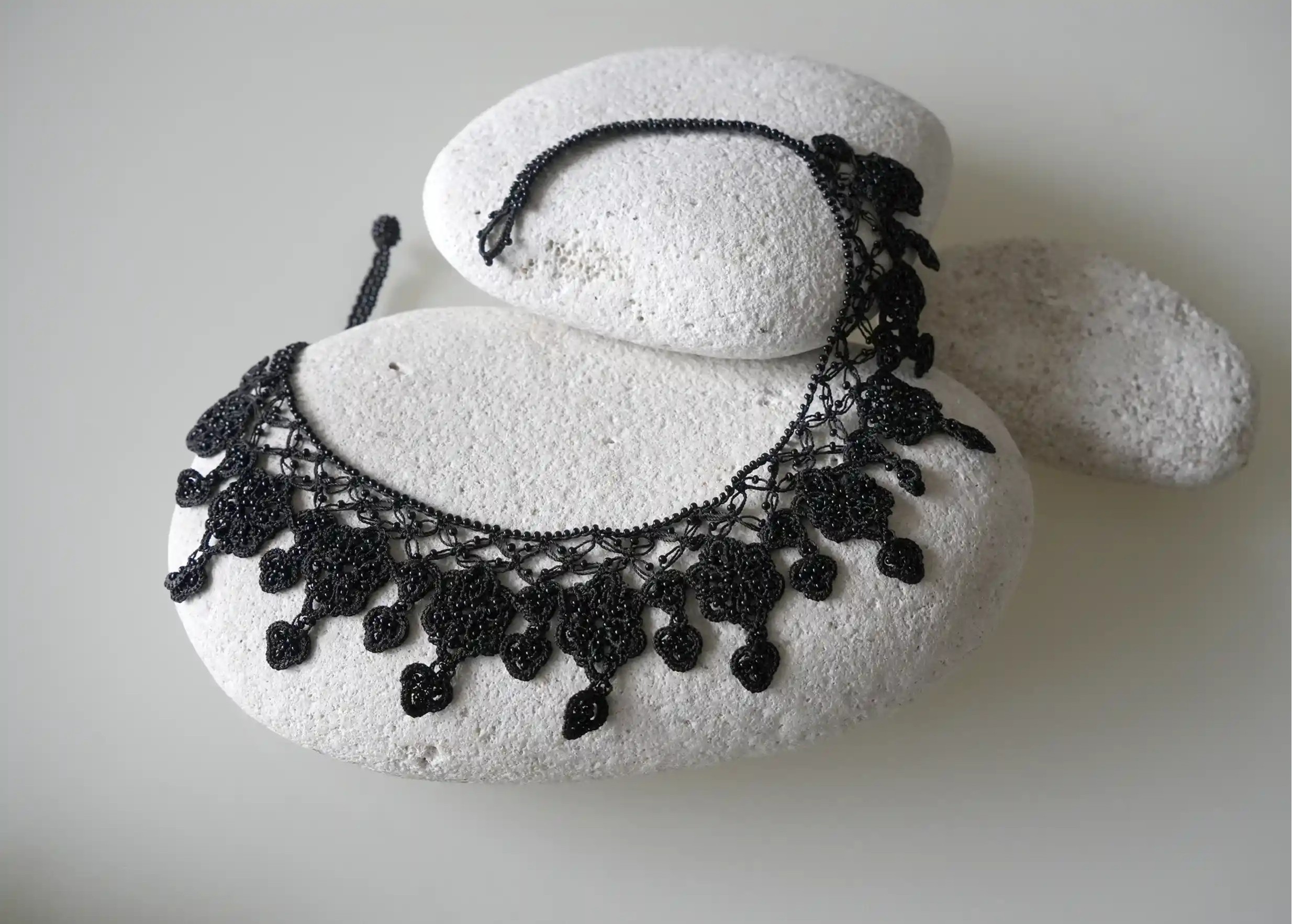 Sonya lace necklace by Karawan, in black, placed on pebbles