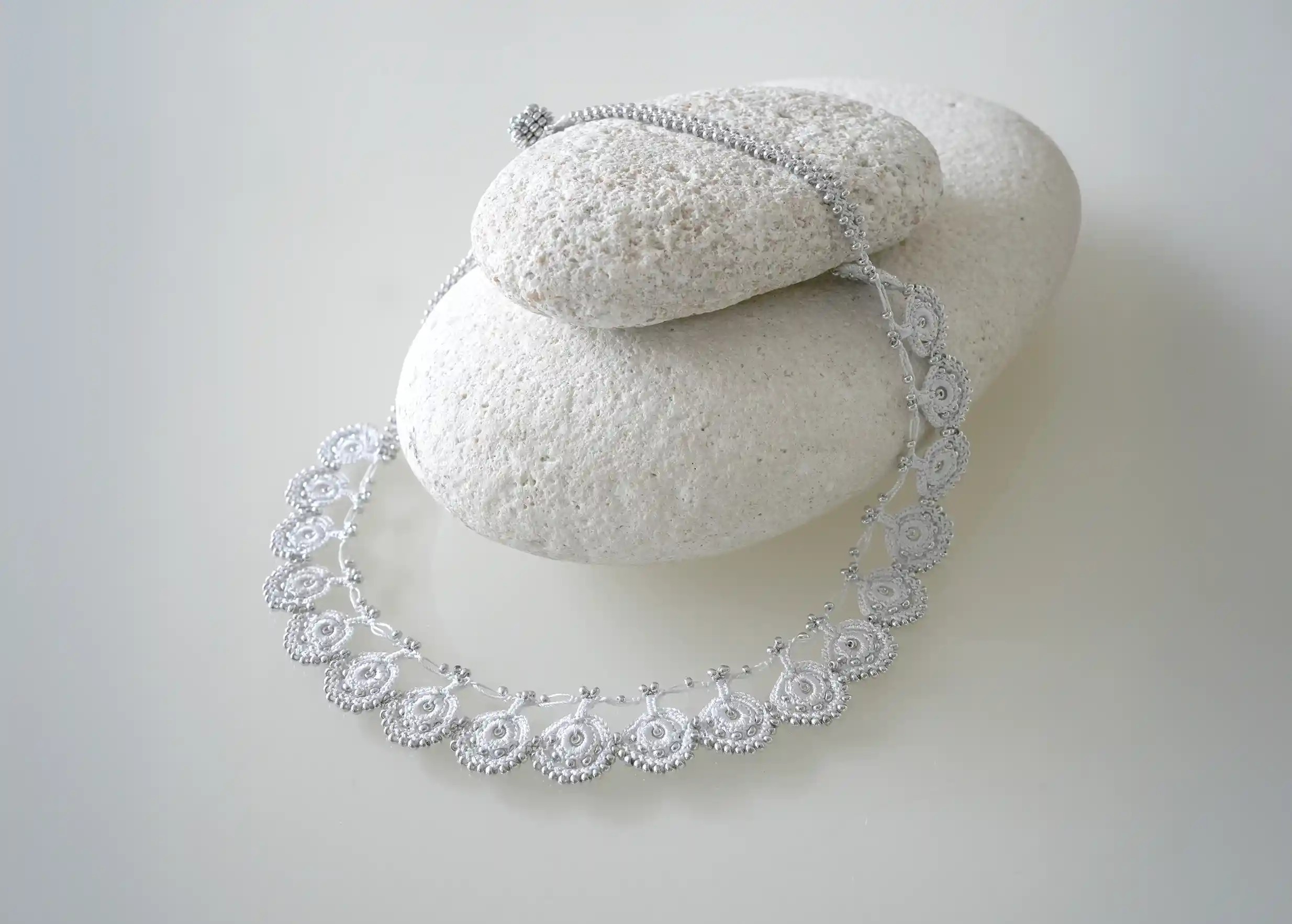 Collier Eda coloris gris argent de la collection Oya posé sur des galets gris clair