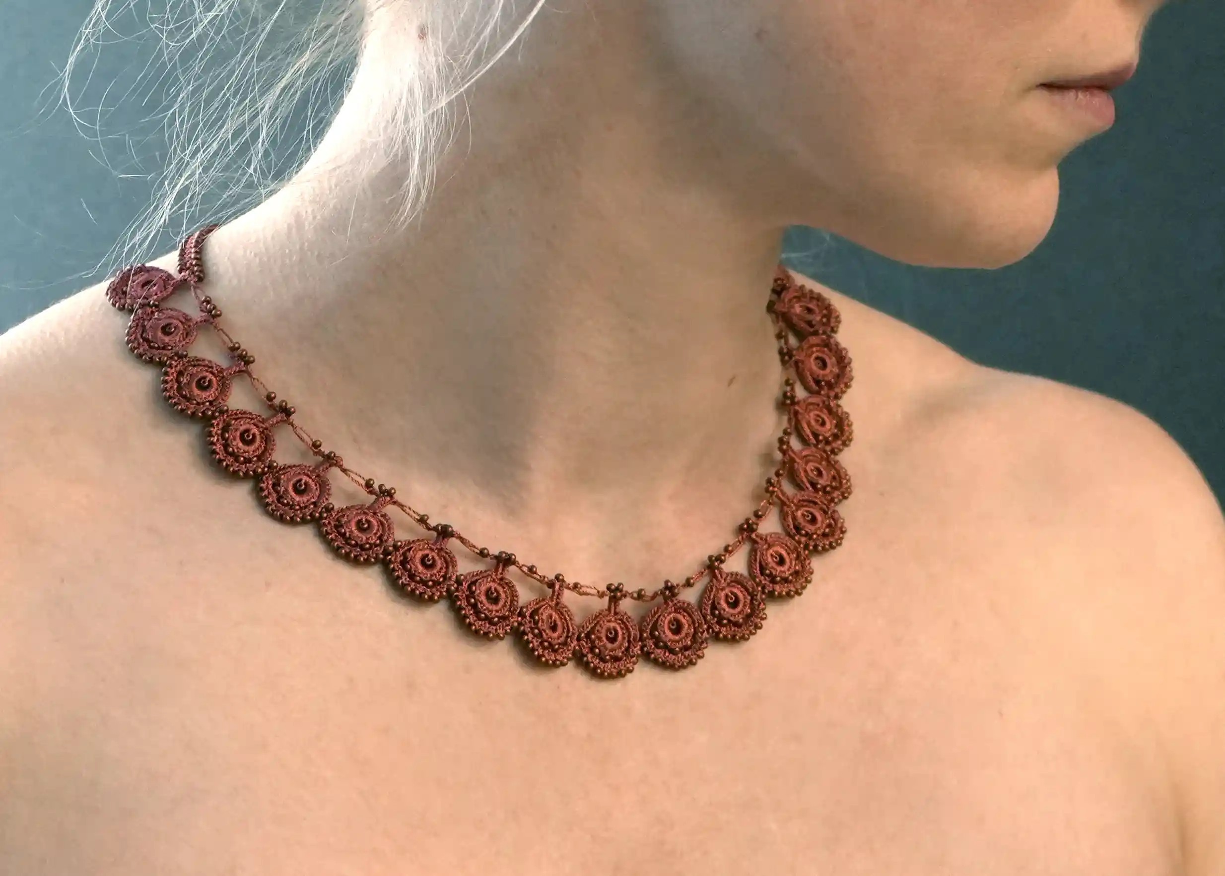 Matt copper-colored lace necklace worn by a person, close-up view