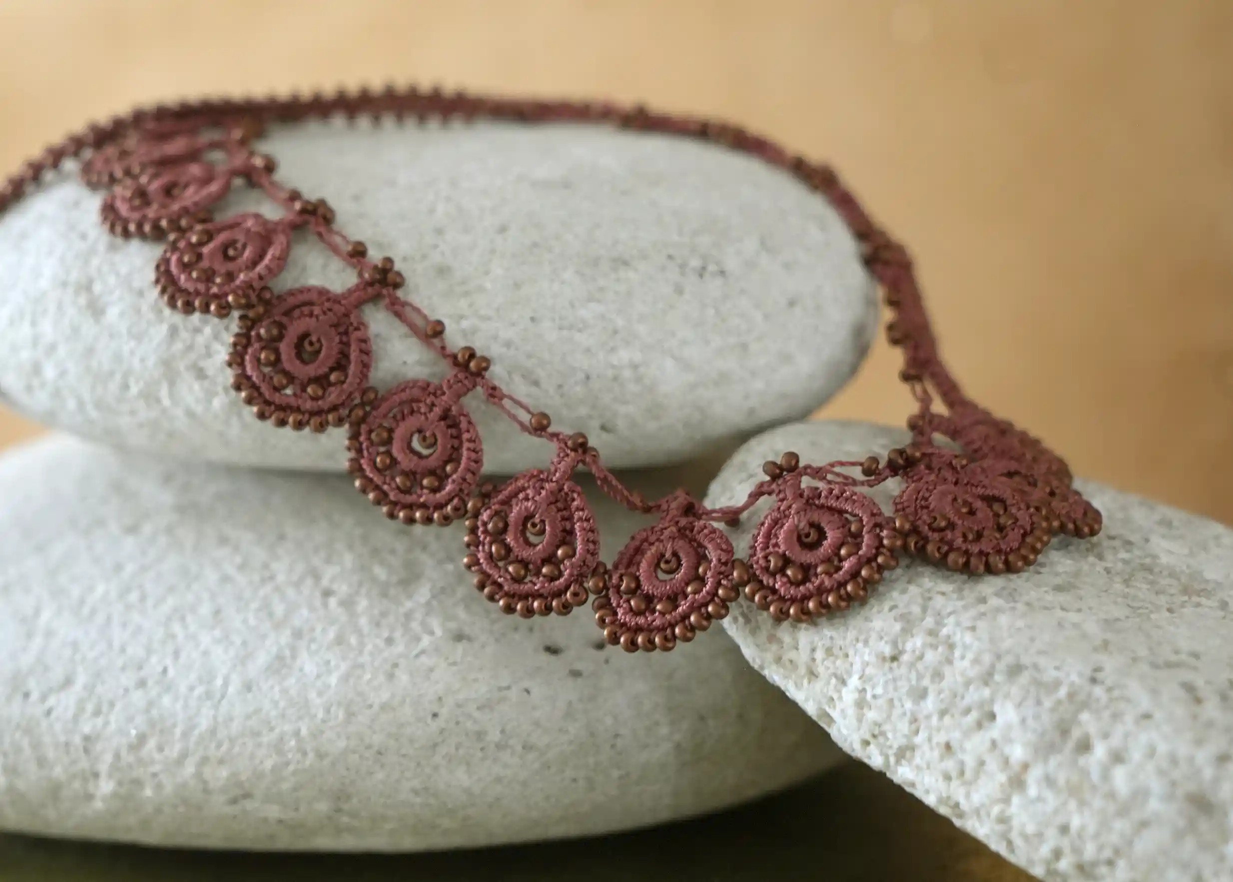 Collier Eda cuivre mat en dentelle Oya posé sur des galets