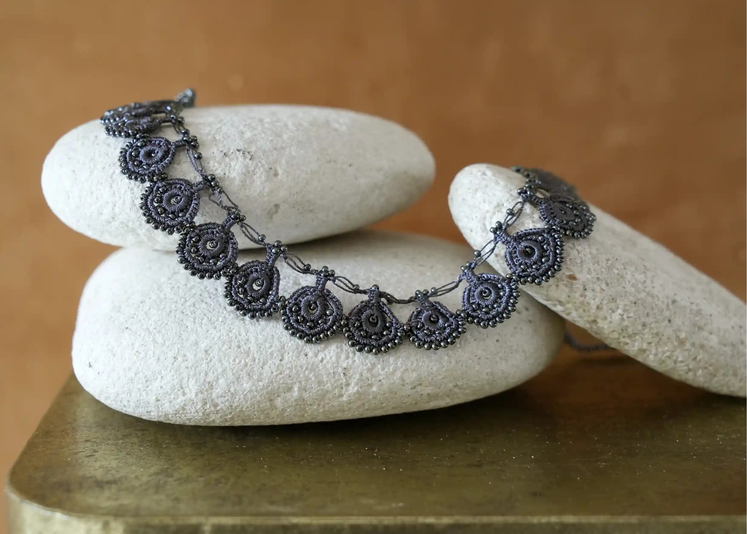 Zoom sur collier Eda coloris bleu ardoise en dentelle Oya posé sur des galets