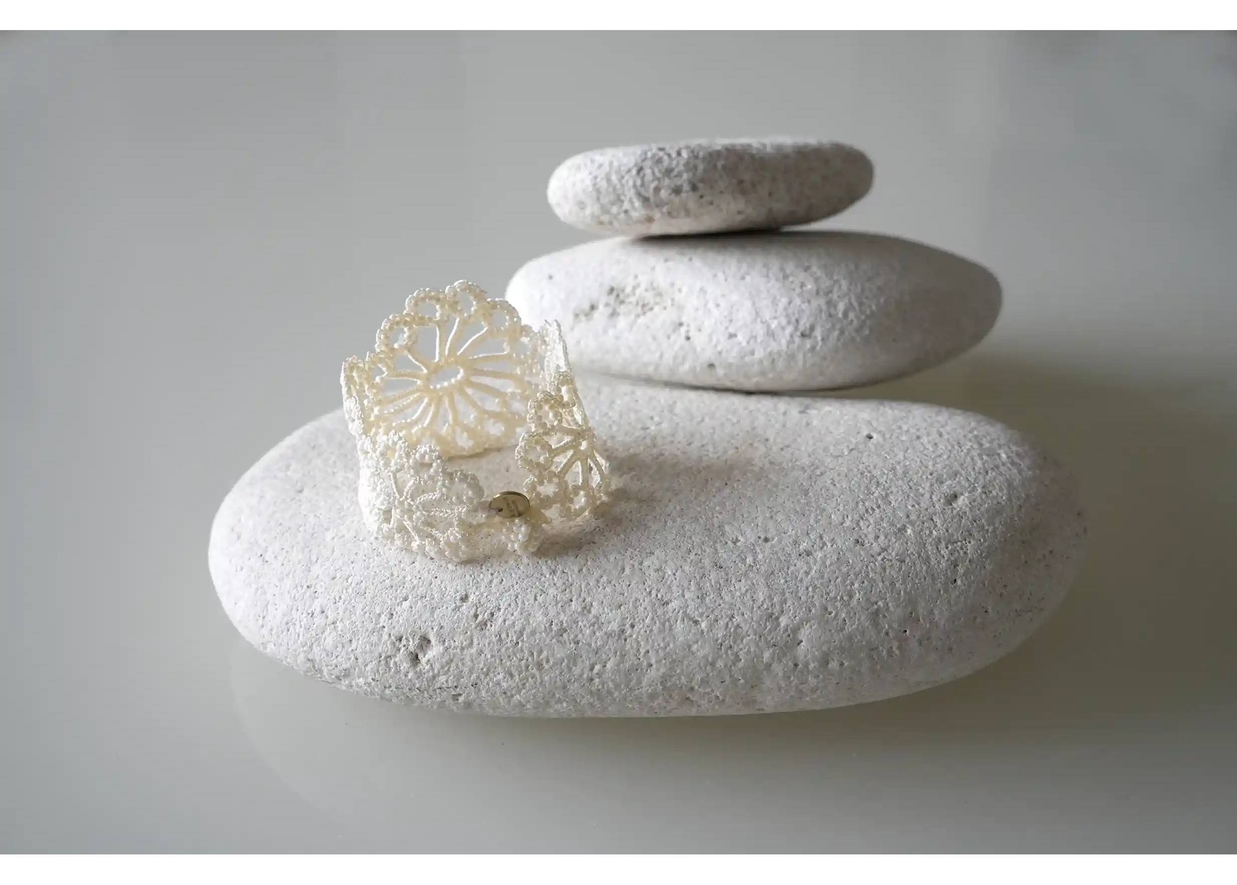 Light ivory Hawa lace bracelet, decorated with pearls, placed on a white pebble