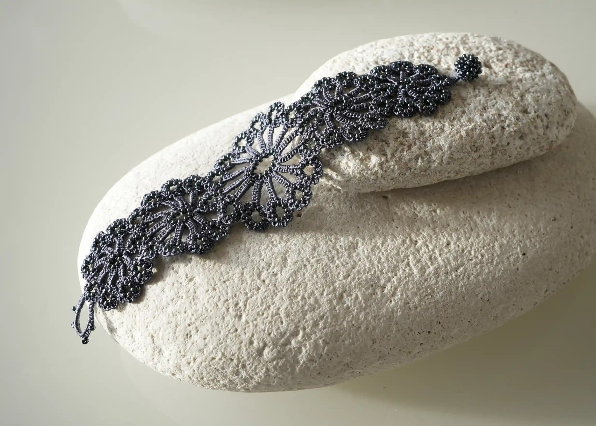 View of the patterns on the slate blue Hawa bracelet, handmade in Turkish lace, placed on a pebble.