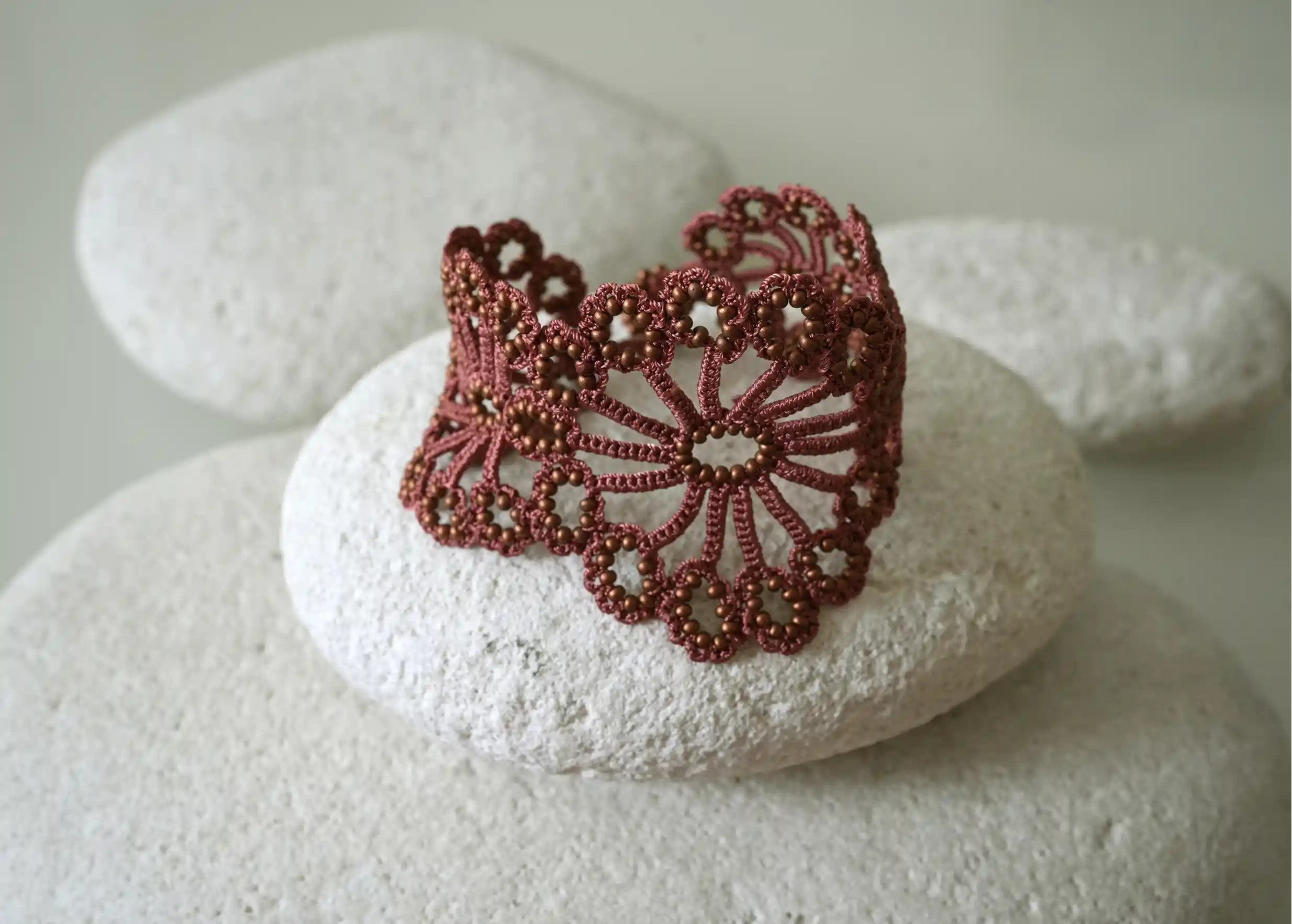 Close-up view of the Matt copper Hawa lace bracelet placed on a white pebble