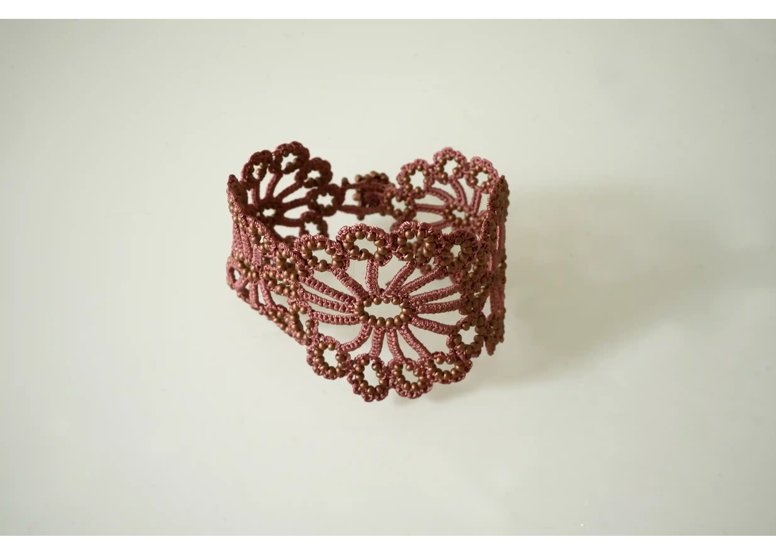 Matt copper Hawa bracelet in handmade lace placed on a white background