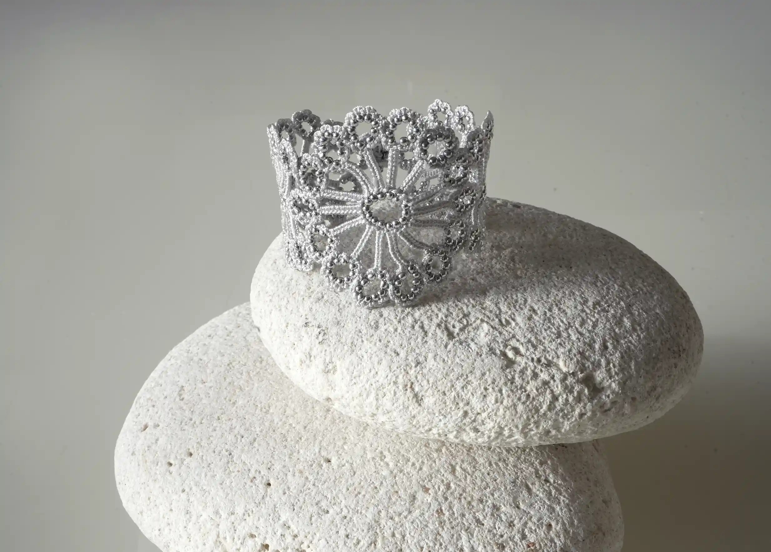 Vue rapprochée du bracelet en dentelle Hawa coloris gris argent posé sur un galet blanc