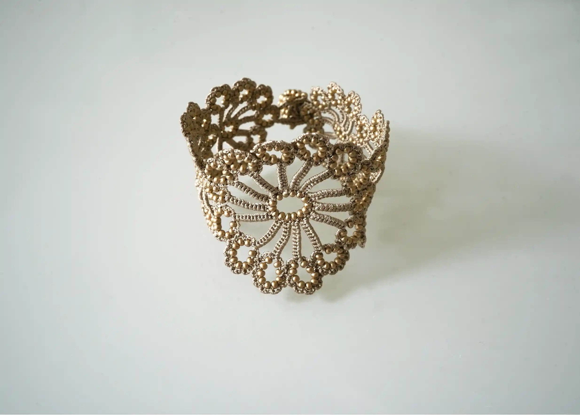 Bracelet en dentelle Hawa or mat, orné de perles, posé sur fond blanc