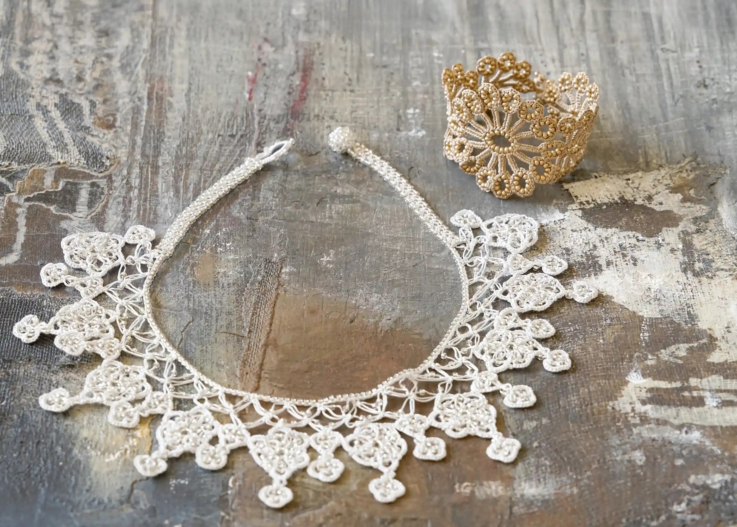 Collier en dentelle Oya posé à plat à côté d'un bracelet beige or