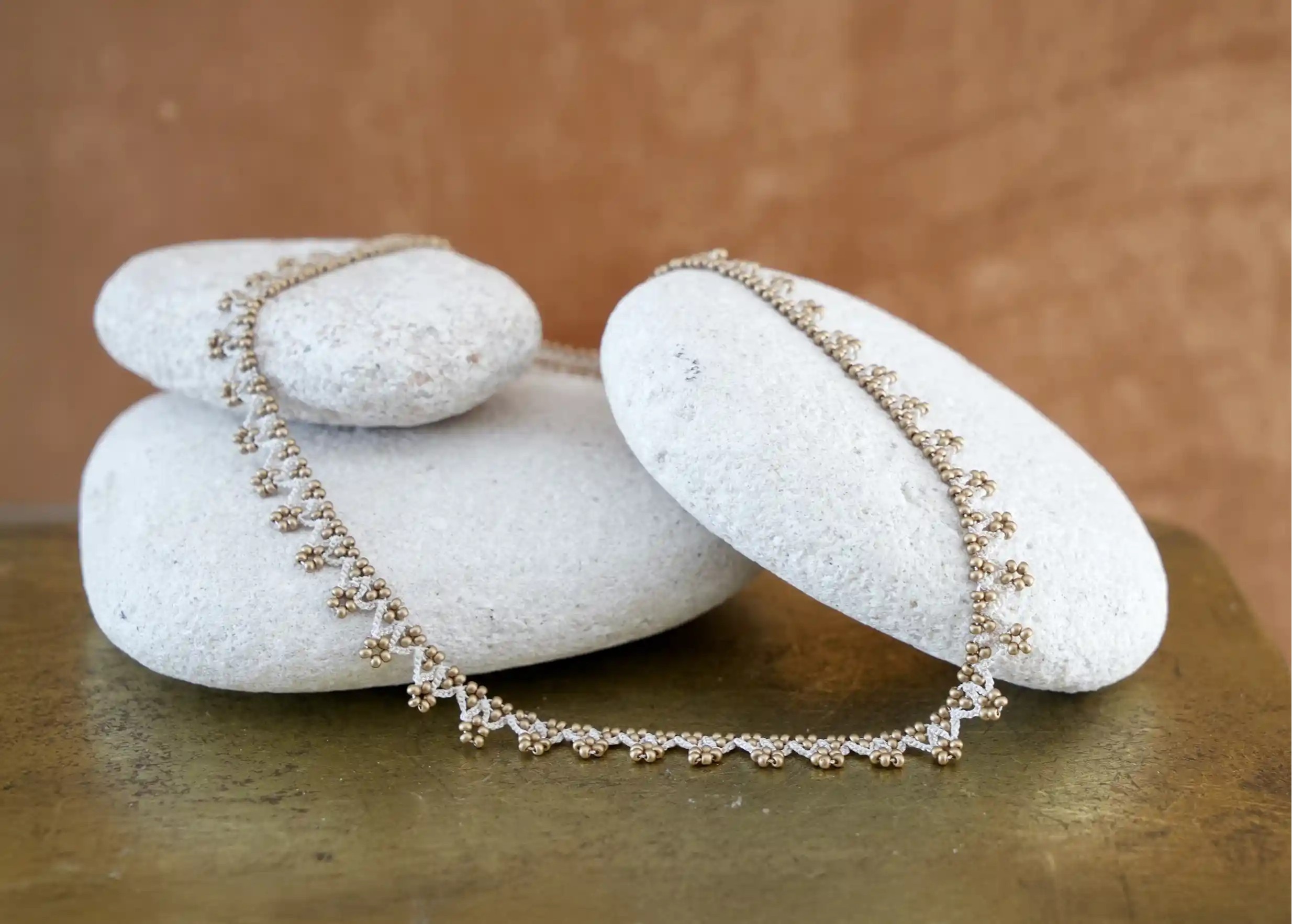 Liana necklace, beige and matte gold, photographed on a pebble