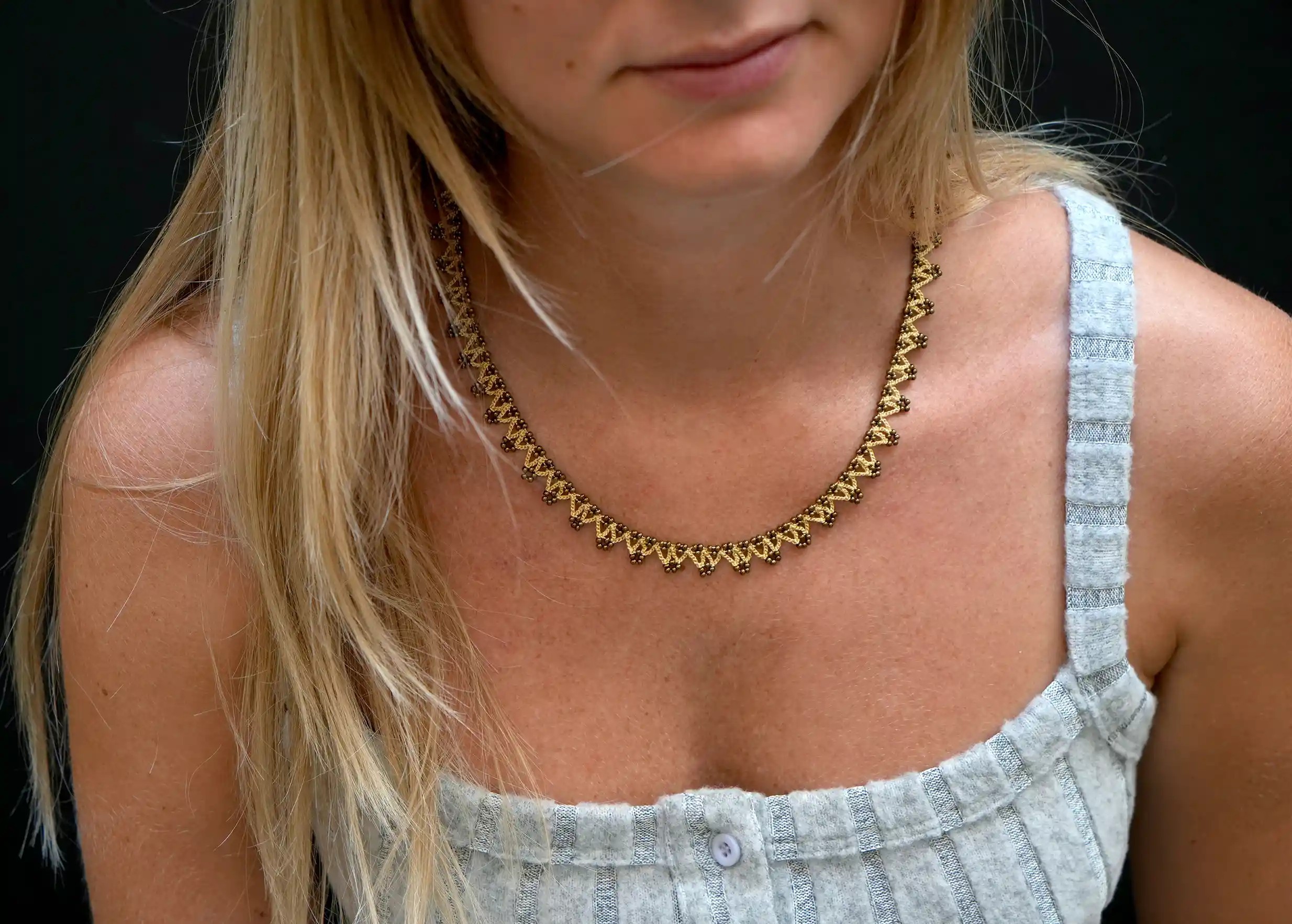 Jeune femme portant au cou un collier textile coloris beige, or et cuivre
