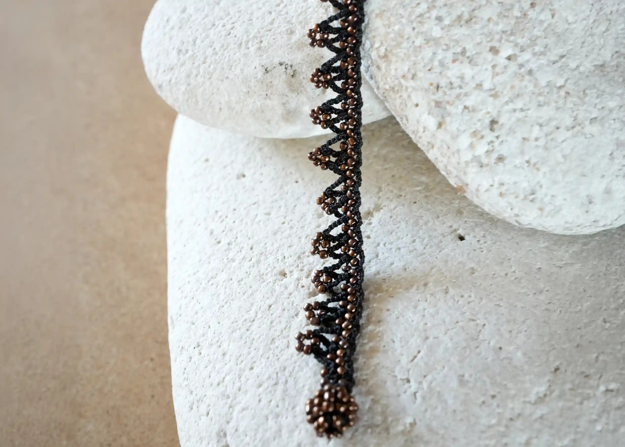Close-up of the details of the “Liana” lace necklace, black and bronze colours