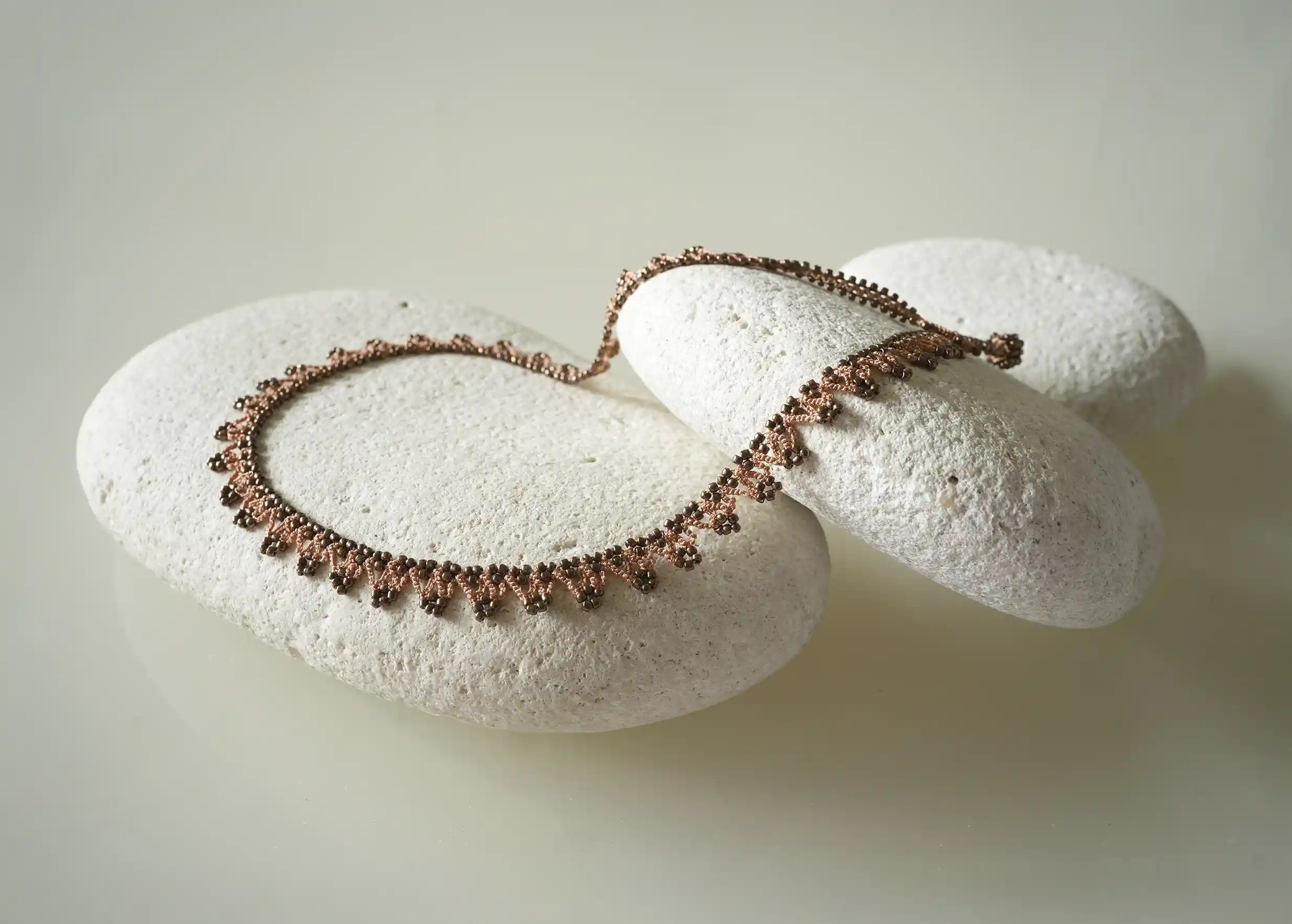 Textile necklace delicately placed on a pebble, terracotta and copper colours