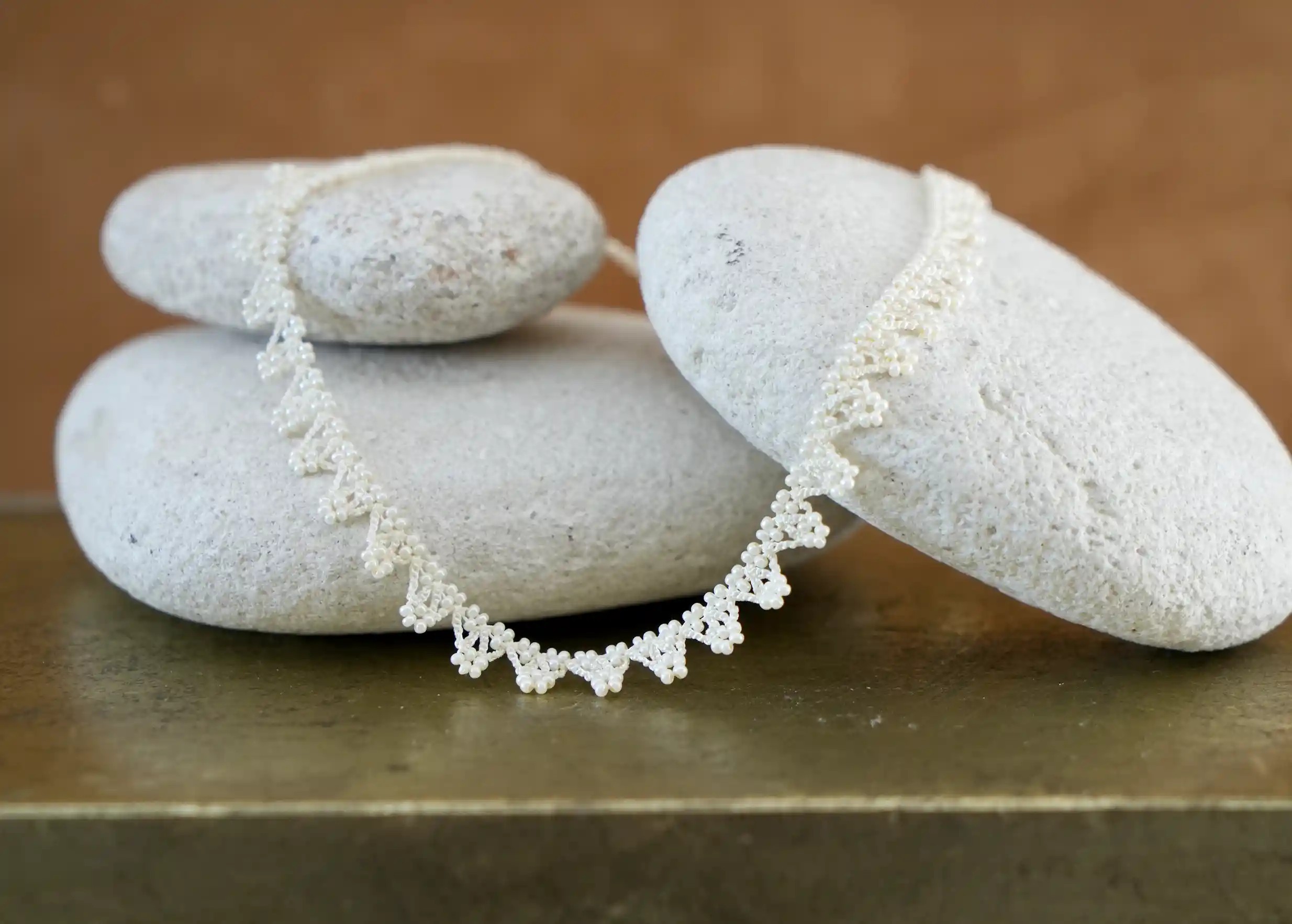 Collier textile délicatement posé sur un galet, coloris ivoire clair