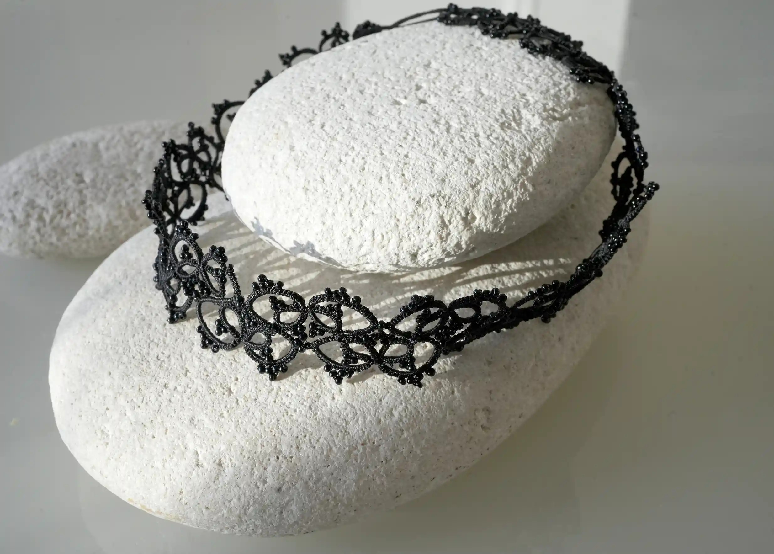 Collier ras de cou Choker en dentelle coloris noir posé sur un galet
