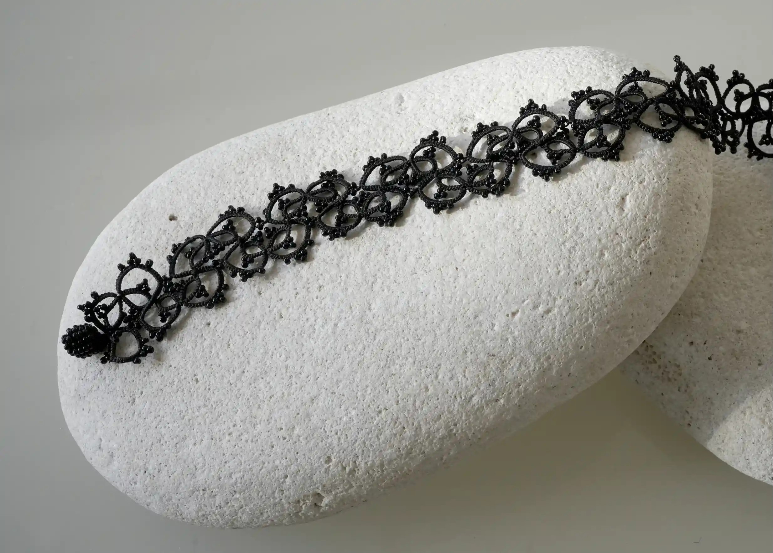 Zoom sur les détails du collier ras de cou Choker en dentelle coloris noir posé sur un galet