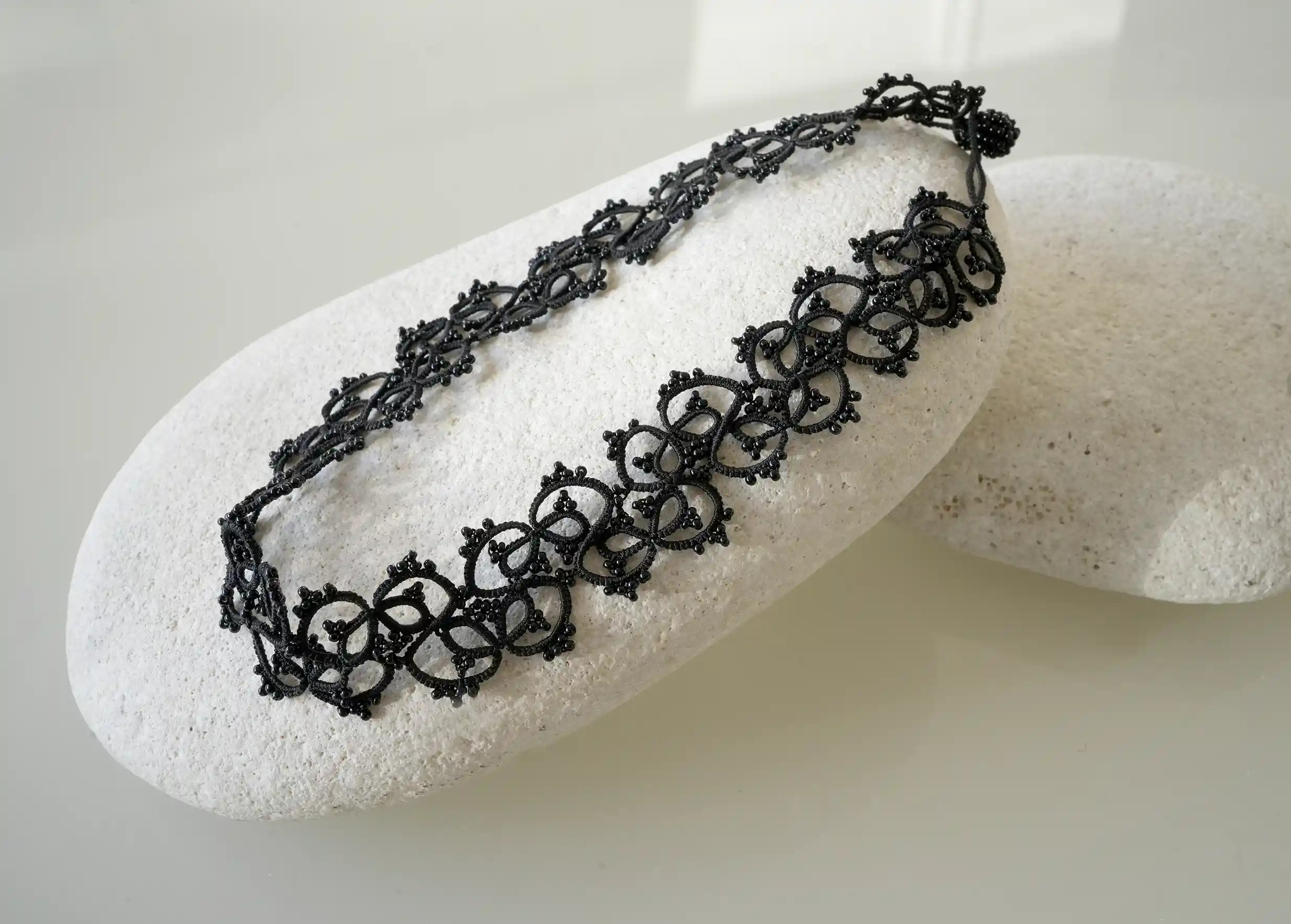 Collier posé délicatement sur un galet, coloris noir et marque Karawan authentic