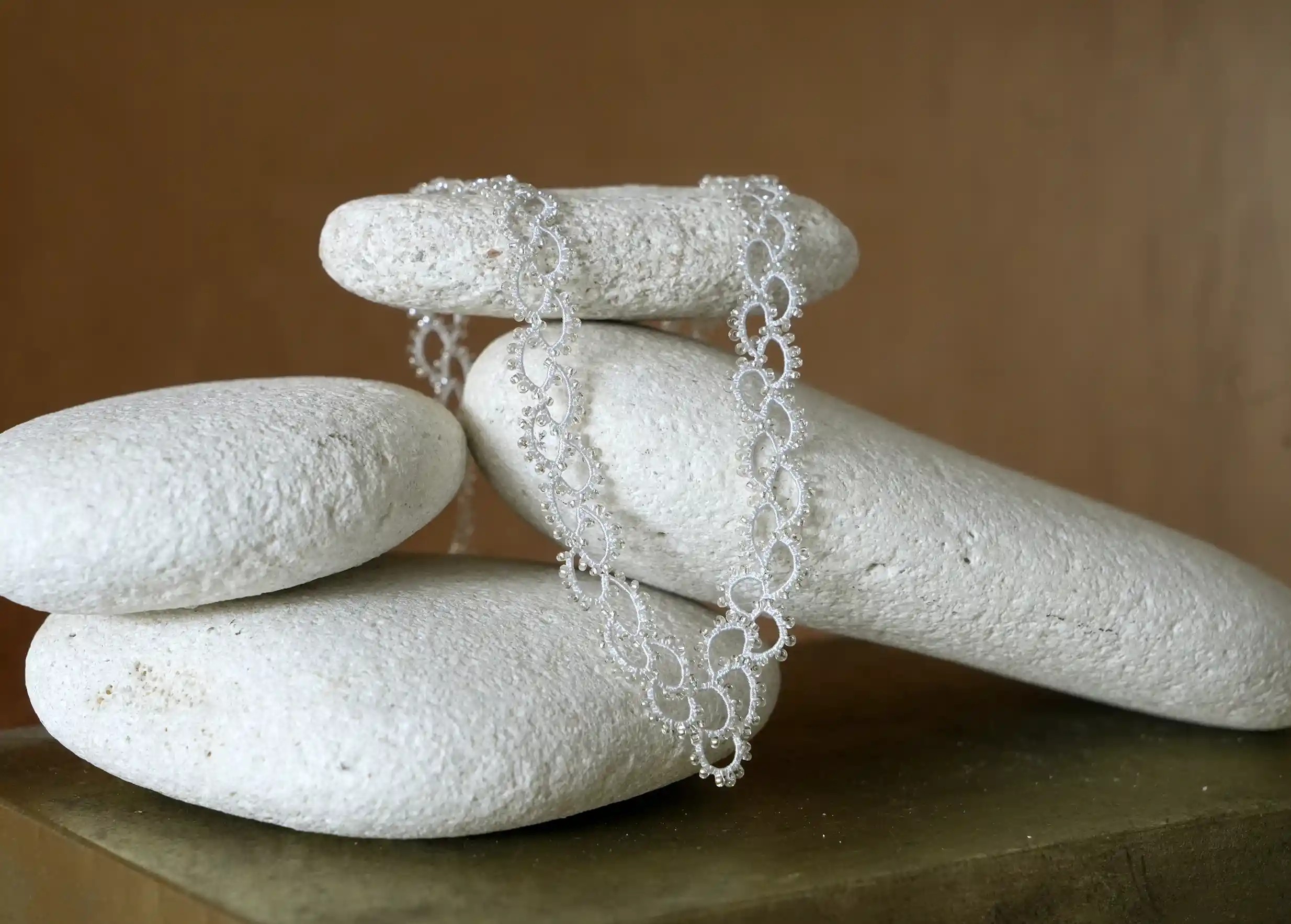Collier en dentelle et perles réalisé à la main, modèle Seed et coloris gris argent, posé sur un galet