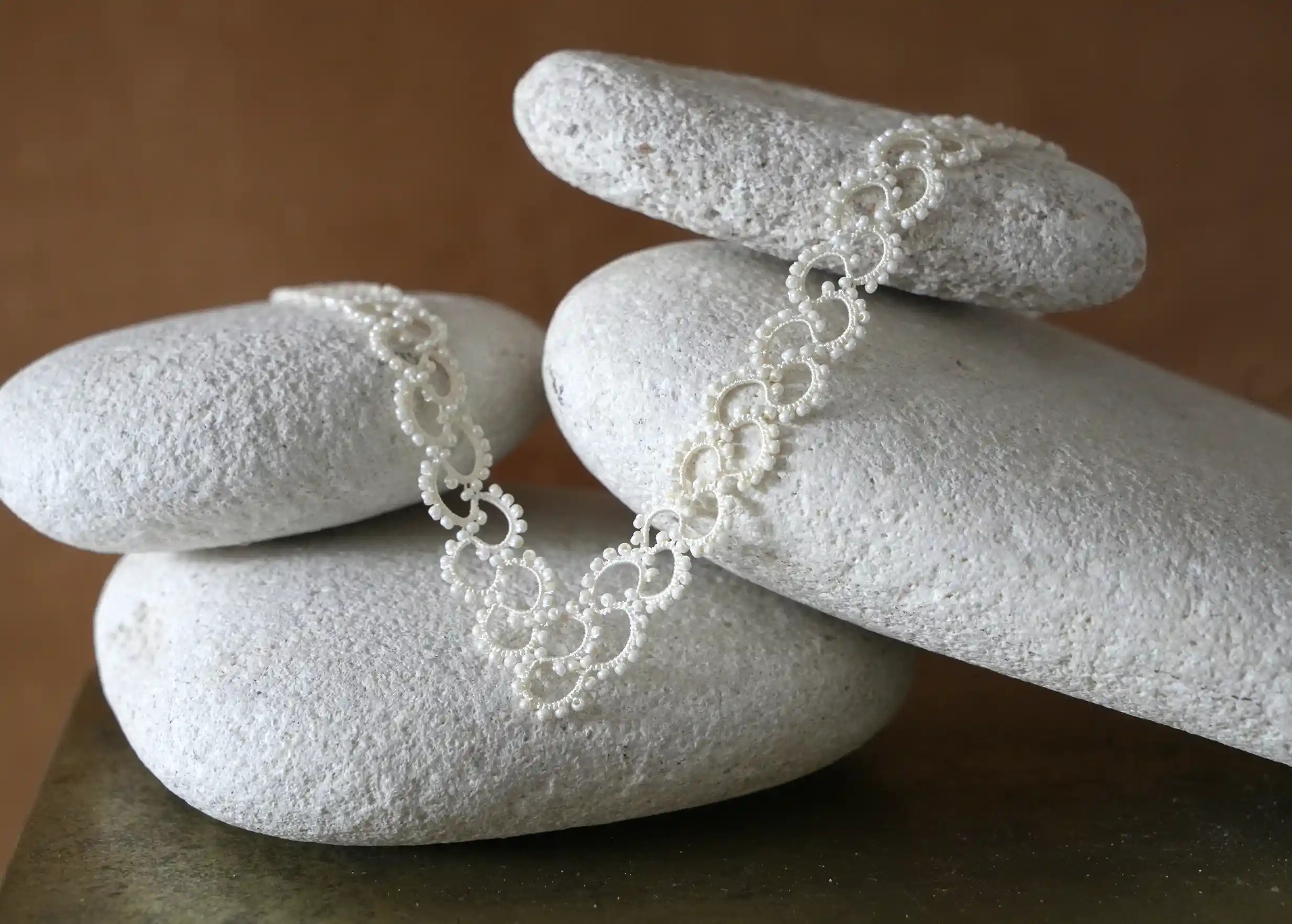 Collier en dentelle et perles réalisé à la main, modèle Seed et coloris ivoire clair, posé sur un galet