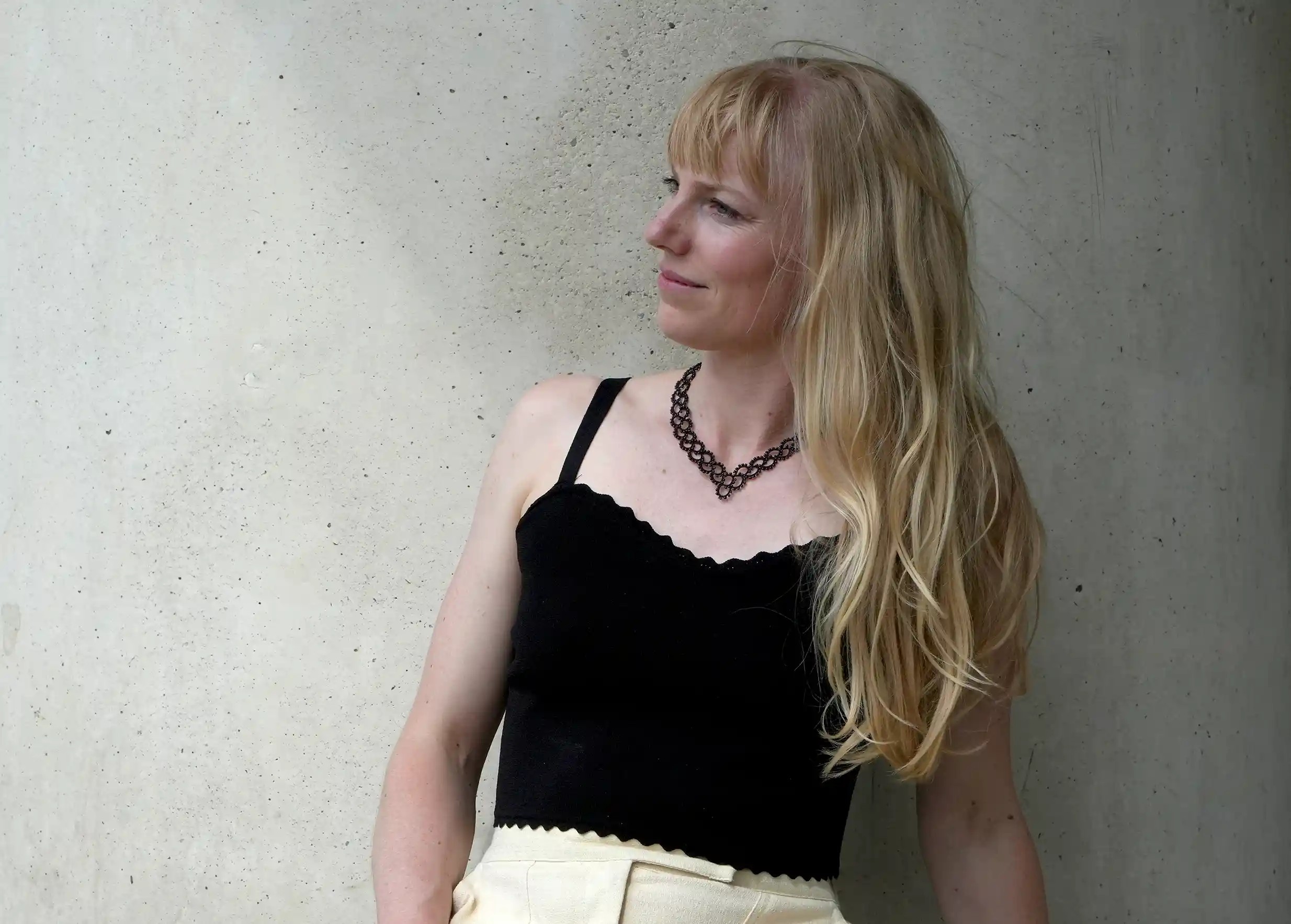 Femme regardant au loin portant un collier en dentelle et perles réalisé à la main, modèle Seed et coloris noir