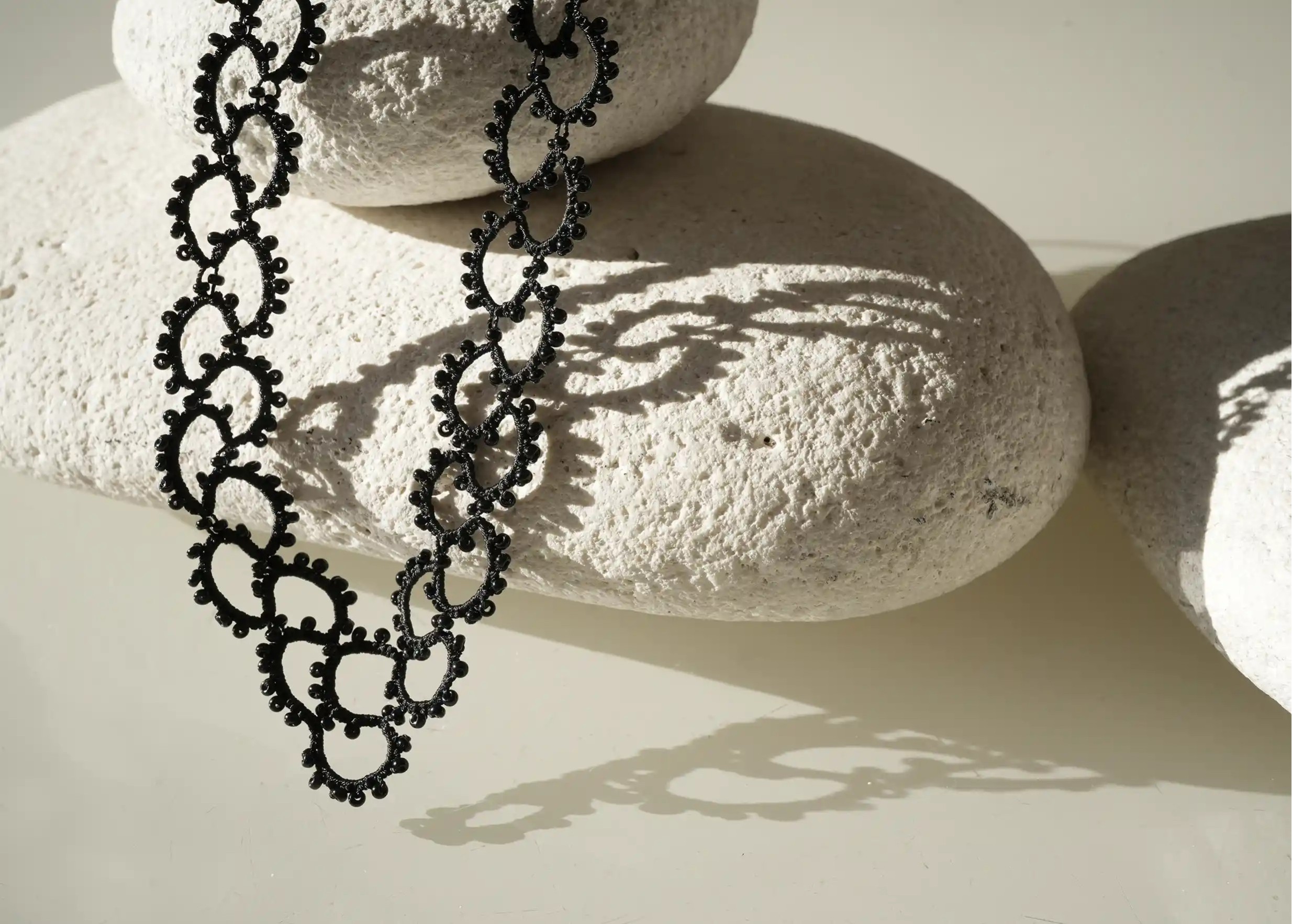 Handmade lace and pearl necklace, Seed model in black, set on a pebble