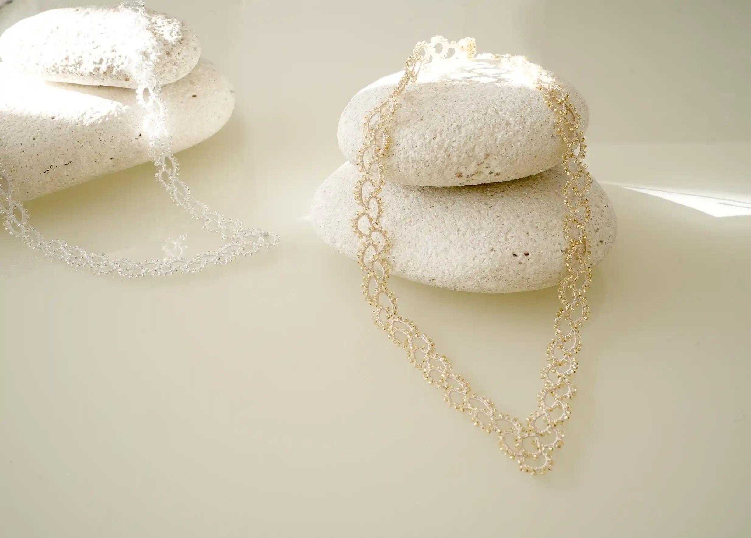 Handmade lace and pearl necklace, Seed model, transparent colour, set on a pebble