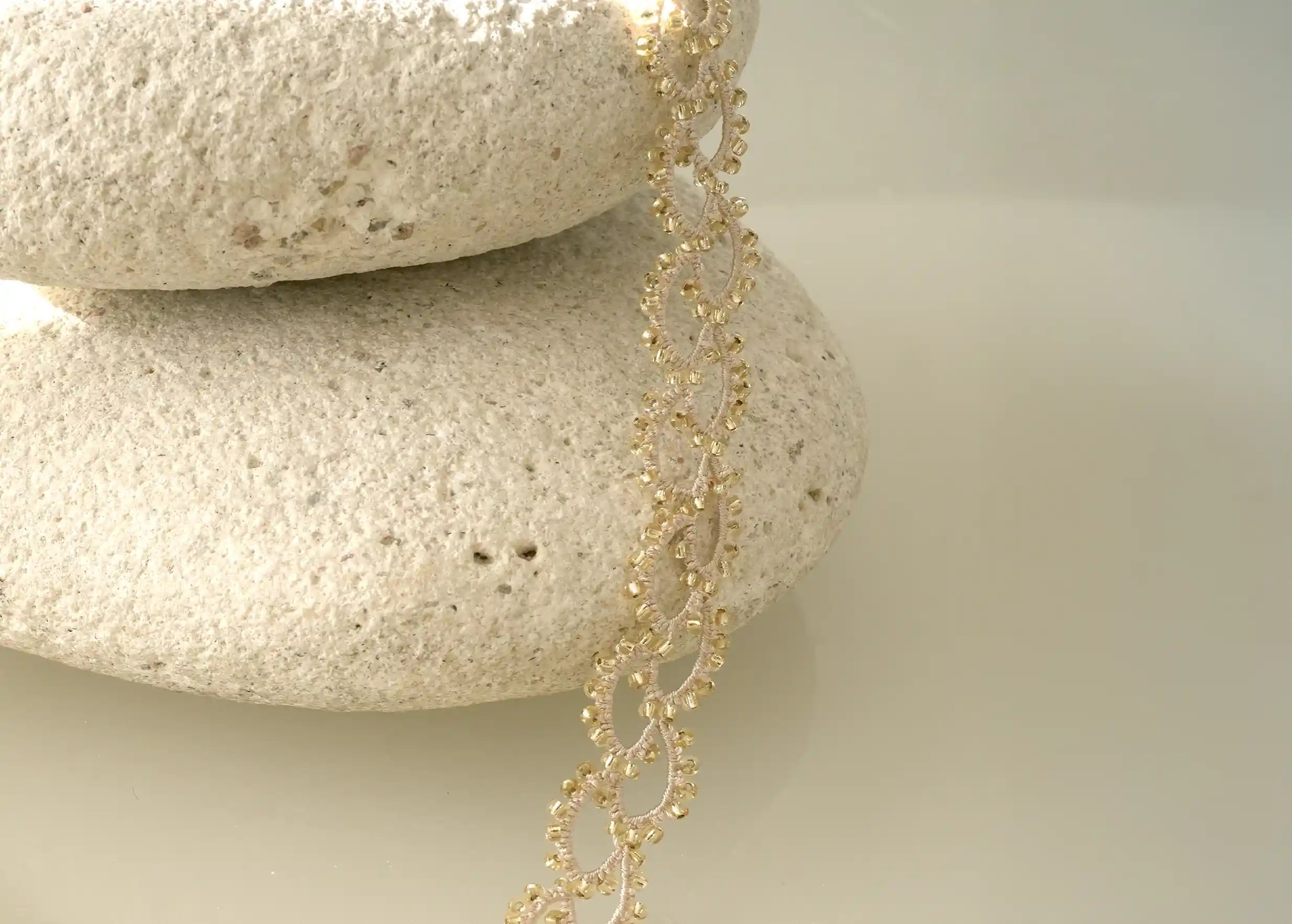 Zoom sur le collier en dentelle et perles réalisé à la main, modèle Seed et coloris or et transparent