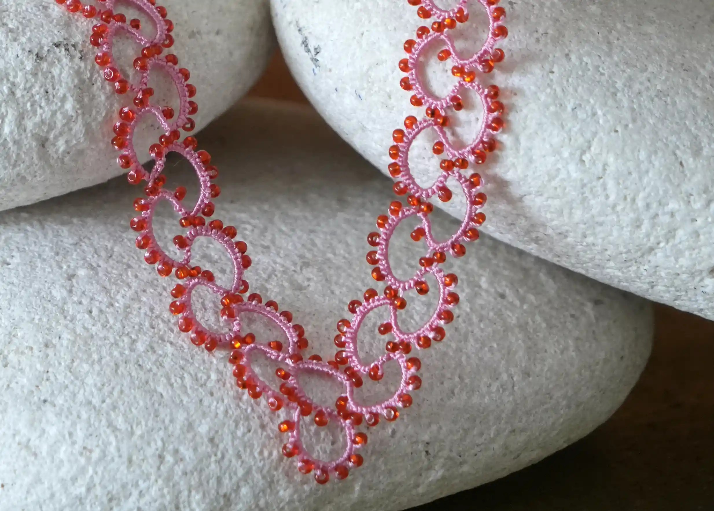 Zoom sur le collier en dentelle et perles réalisé à la main, modèle Seed et coloris rose et rouge