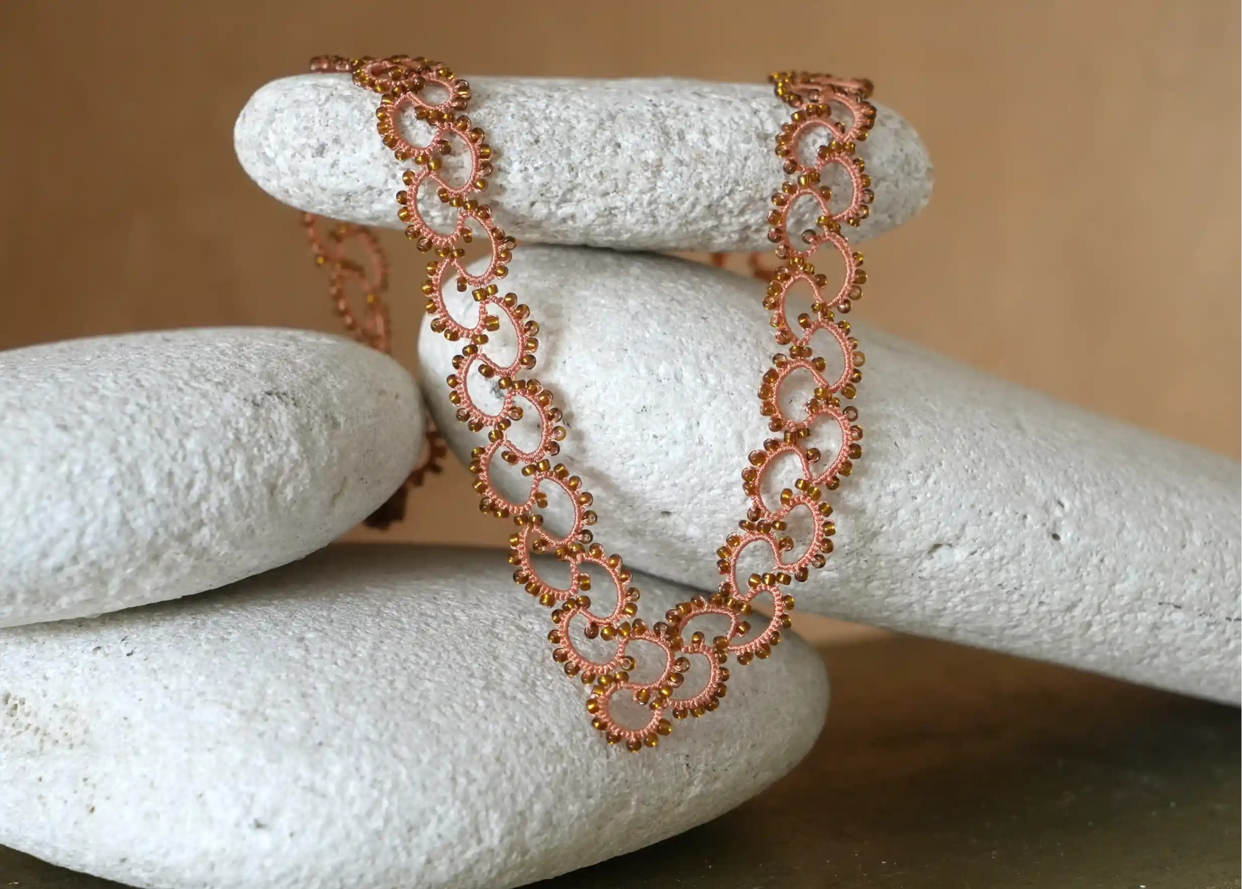Handmade lace and pearl necklace, Seed model in orange and copper colours, set on a pebble