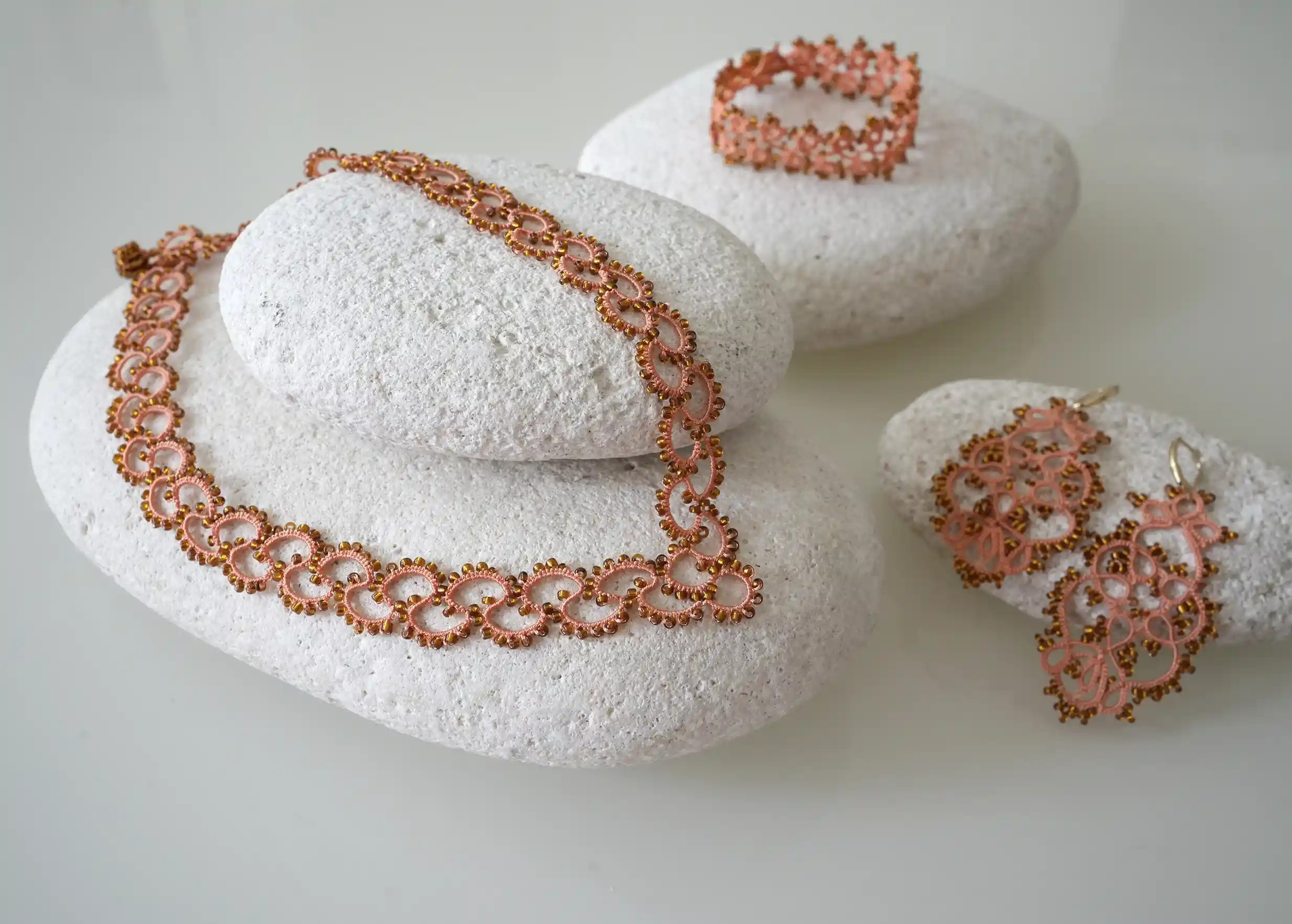 Ensemble de la gamme Seed en dentelle et perles réalisé à la main, coloris orange et cuivre, posé sur un galet
