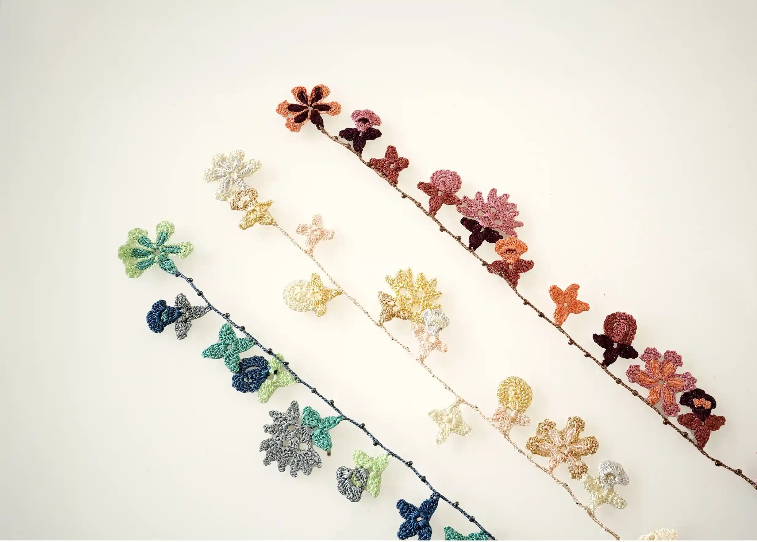 Trio of lace necklaces with floral and leaf motifs, in mother-of-pearl, ocean blue and woody colours