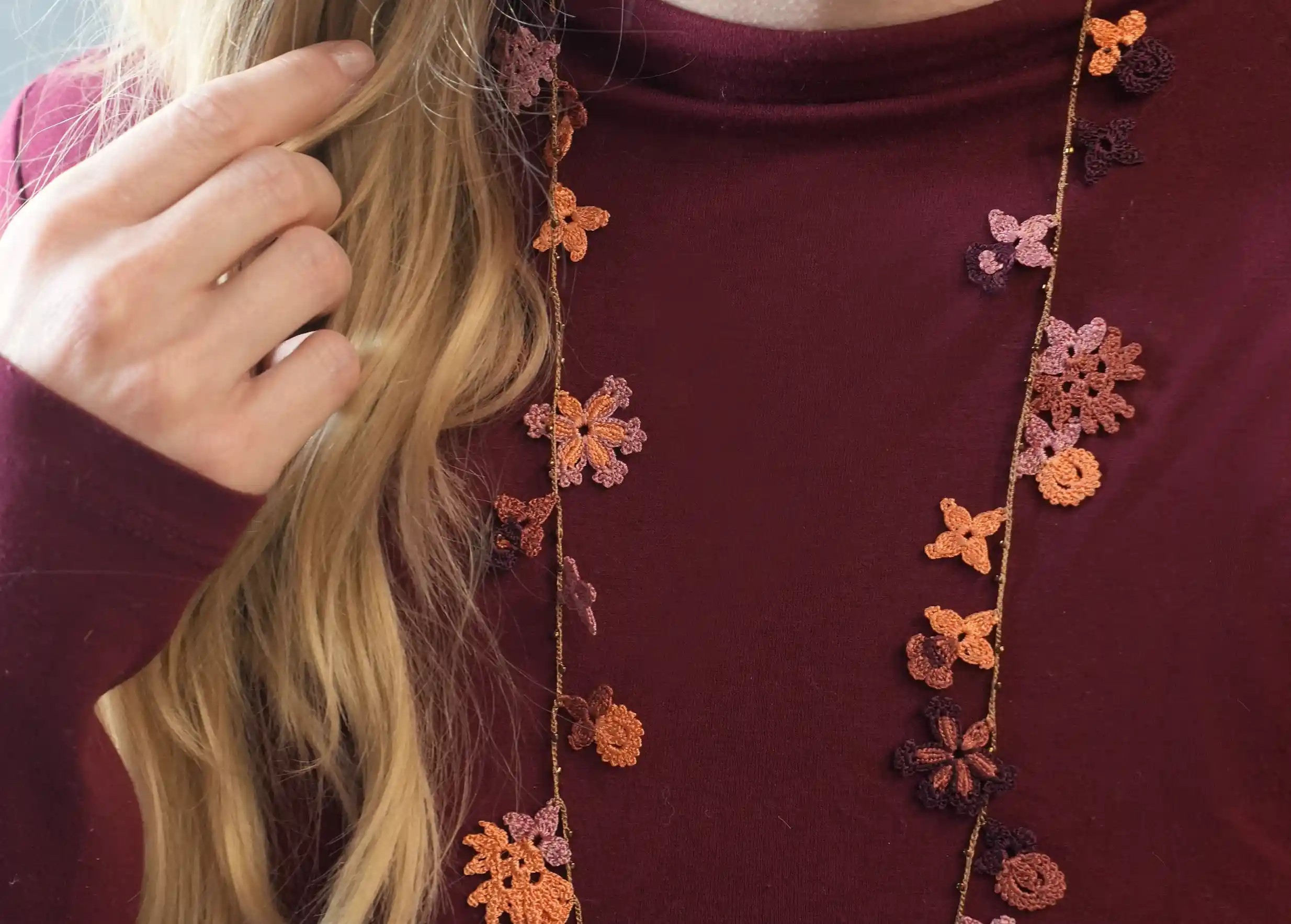 Close-up of the lace necklace worn by a woman, with floral and leaf motifs, Bloom in woody colour