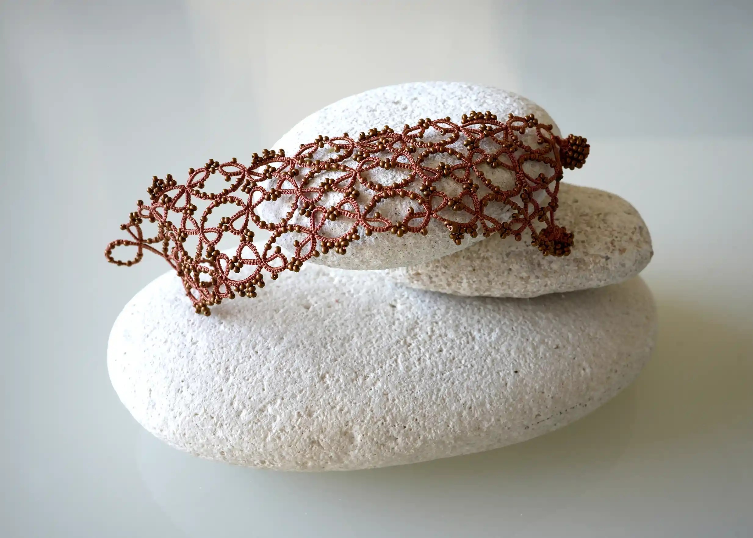 Bracelet manchette large en dentelle délicatement posé sur un galet, modèle Crown