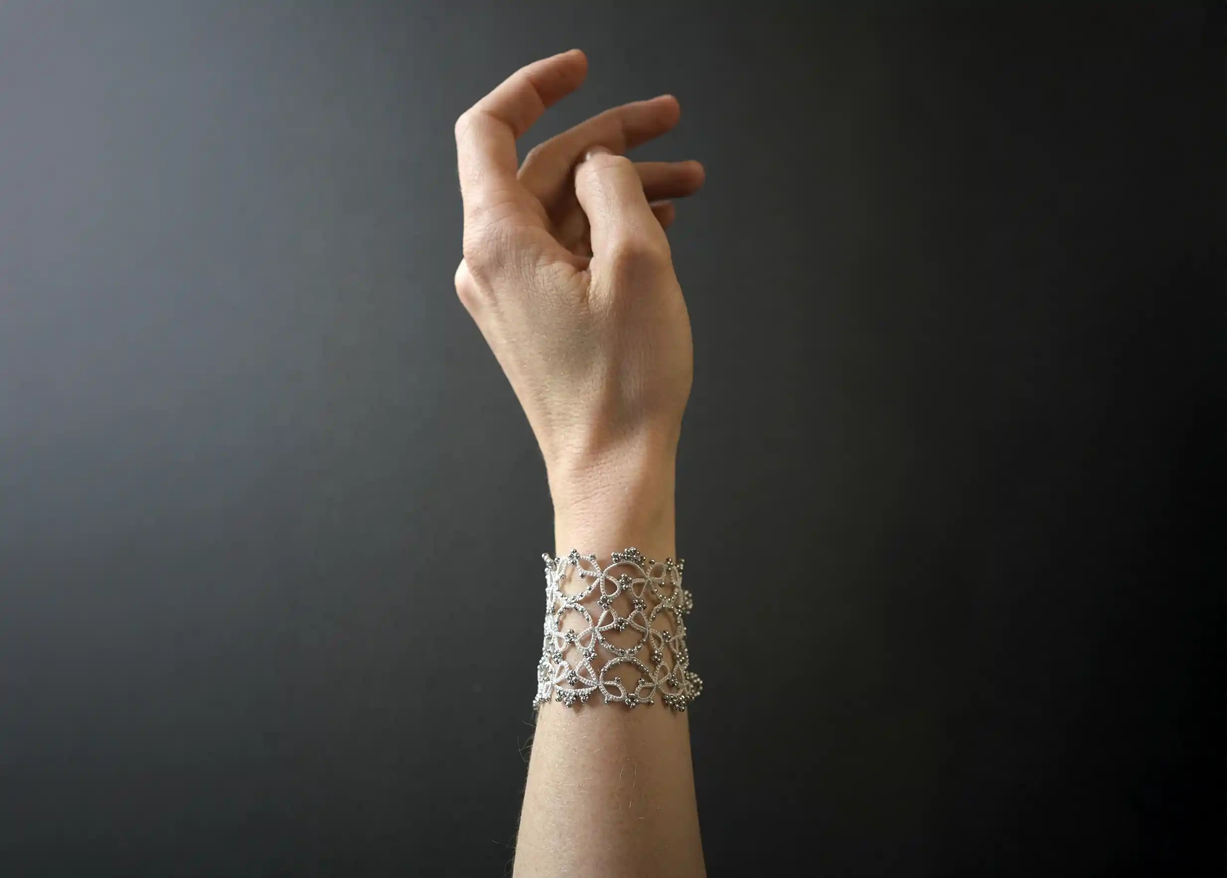Wide lace cuff bracelet worn around the wrist, Crown model in silver grey