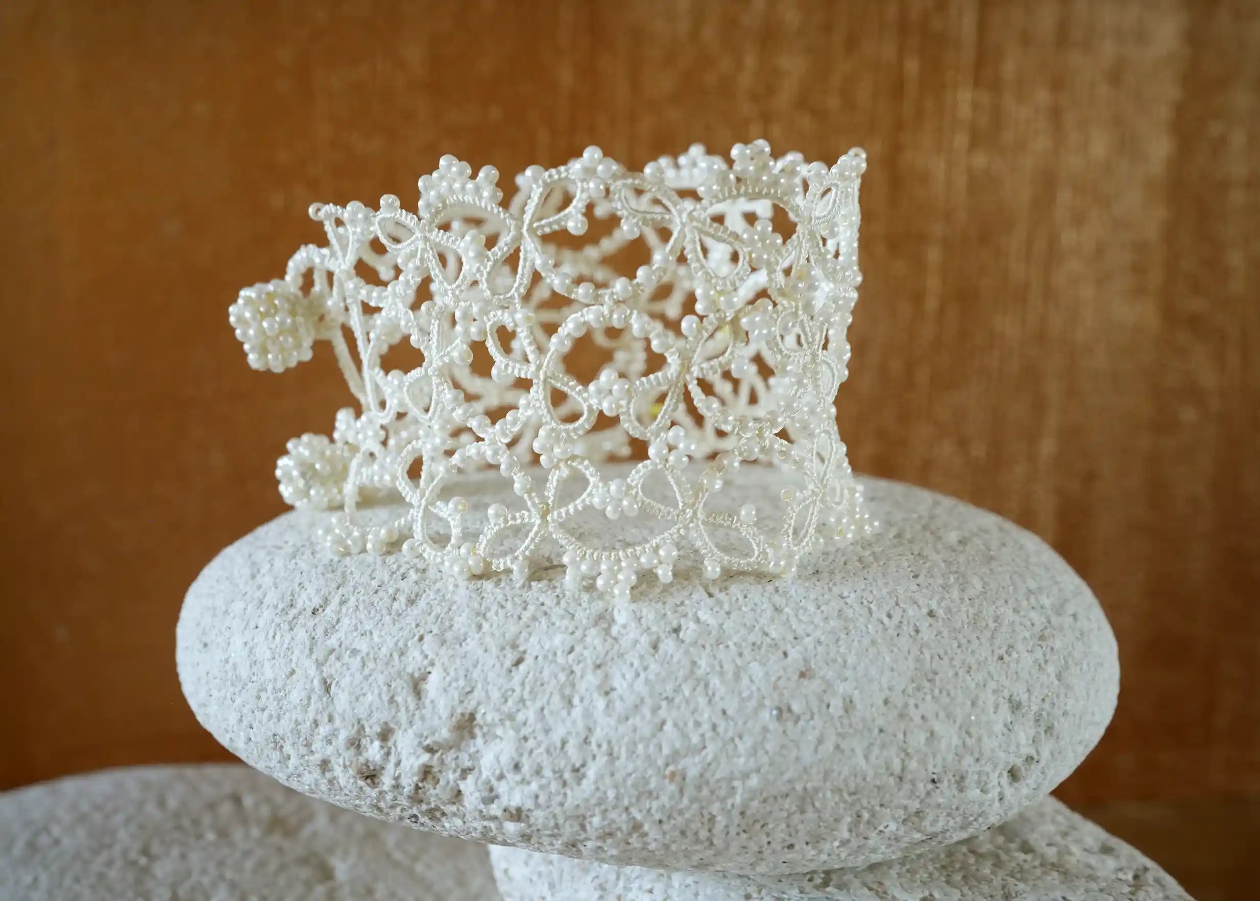 Wide lace cuff bracelet delicately placed on a pebble, Crown model in light ivory colour