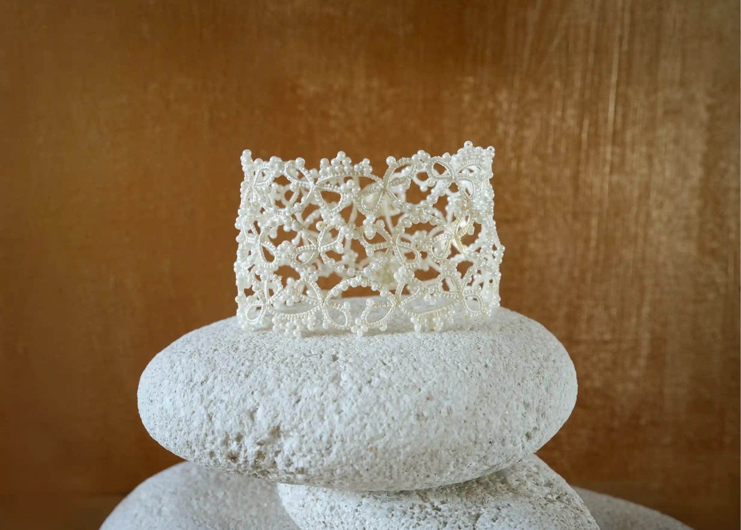 Handmade lace cuff bracelet delicately placed on a pebble, Crown model