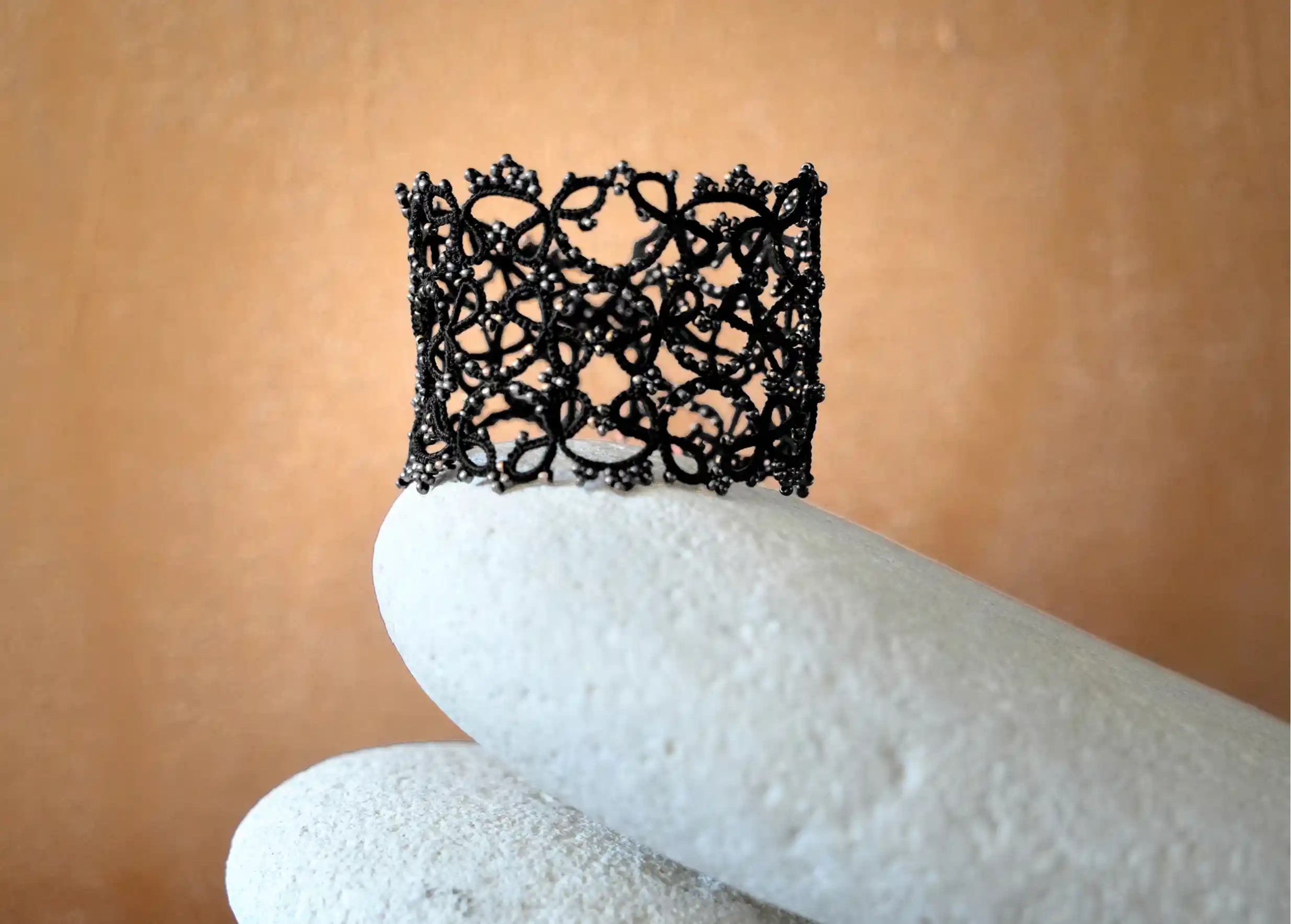Bracelet manchette large en dentelle délicatement posé sur un galet, modèle Crown coloris noir