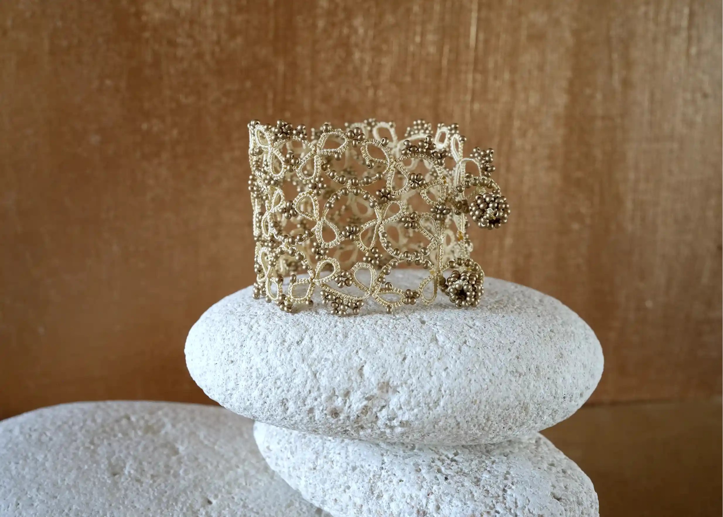 Wide lace cuff bracelet delicately placed on a pebble, Crown model in matt gold colour