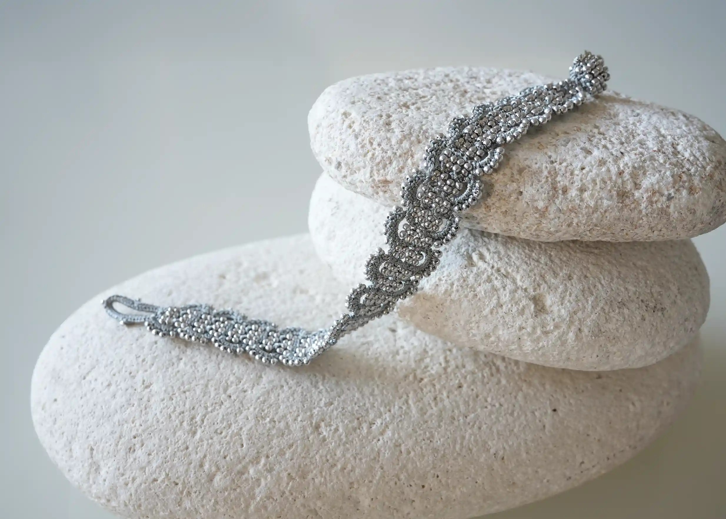 Zoom sur les détails du bracelet en fil et perles coloris bleu glacier et argent posé sur un galet, modèle Bark
