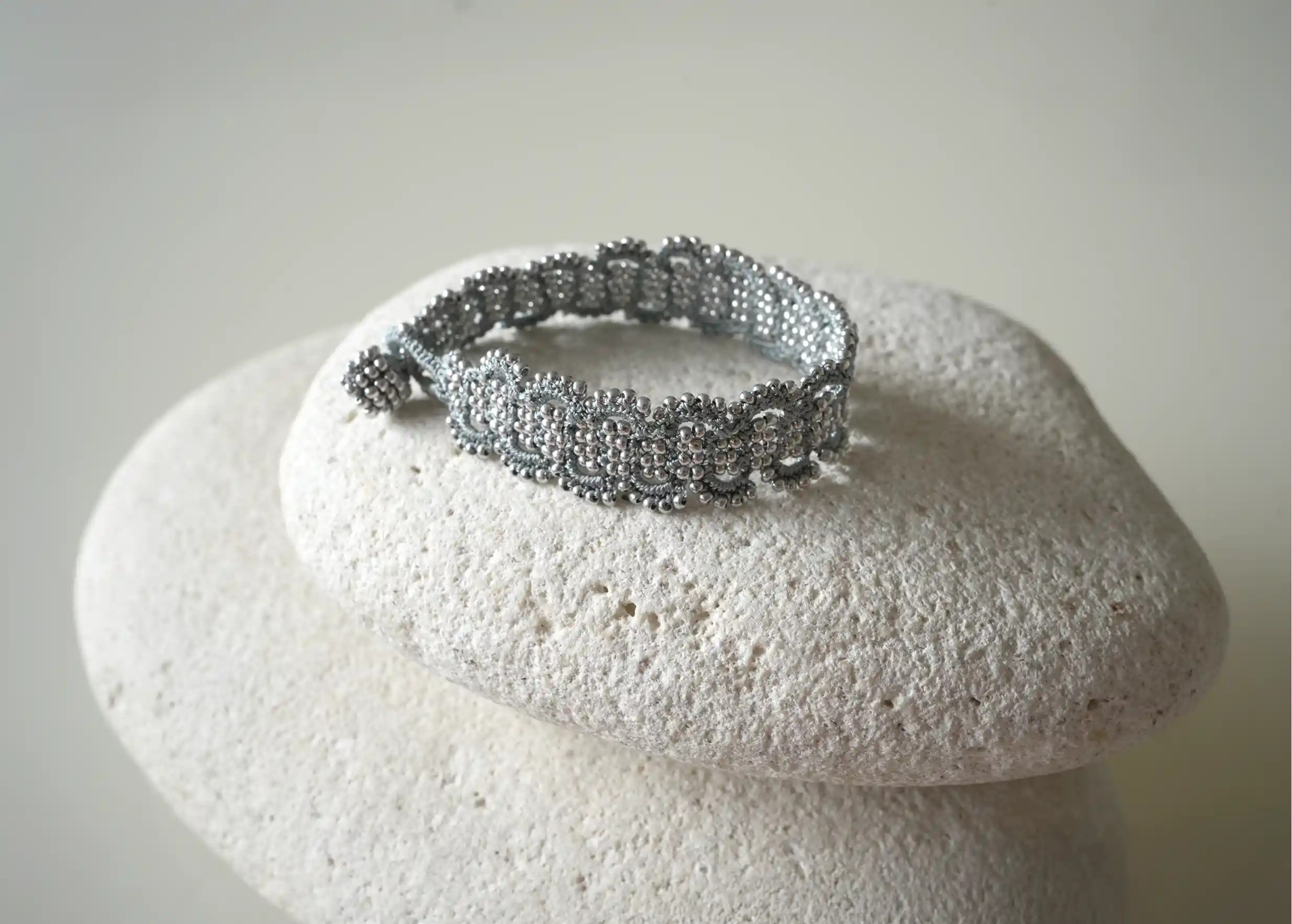 Bracelet en fil et perles coloris bleu glacier et argent posé sur un galet, modèle Bark