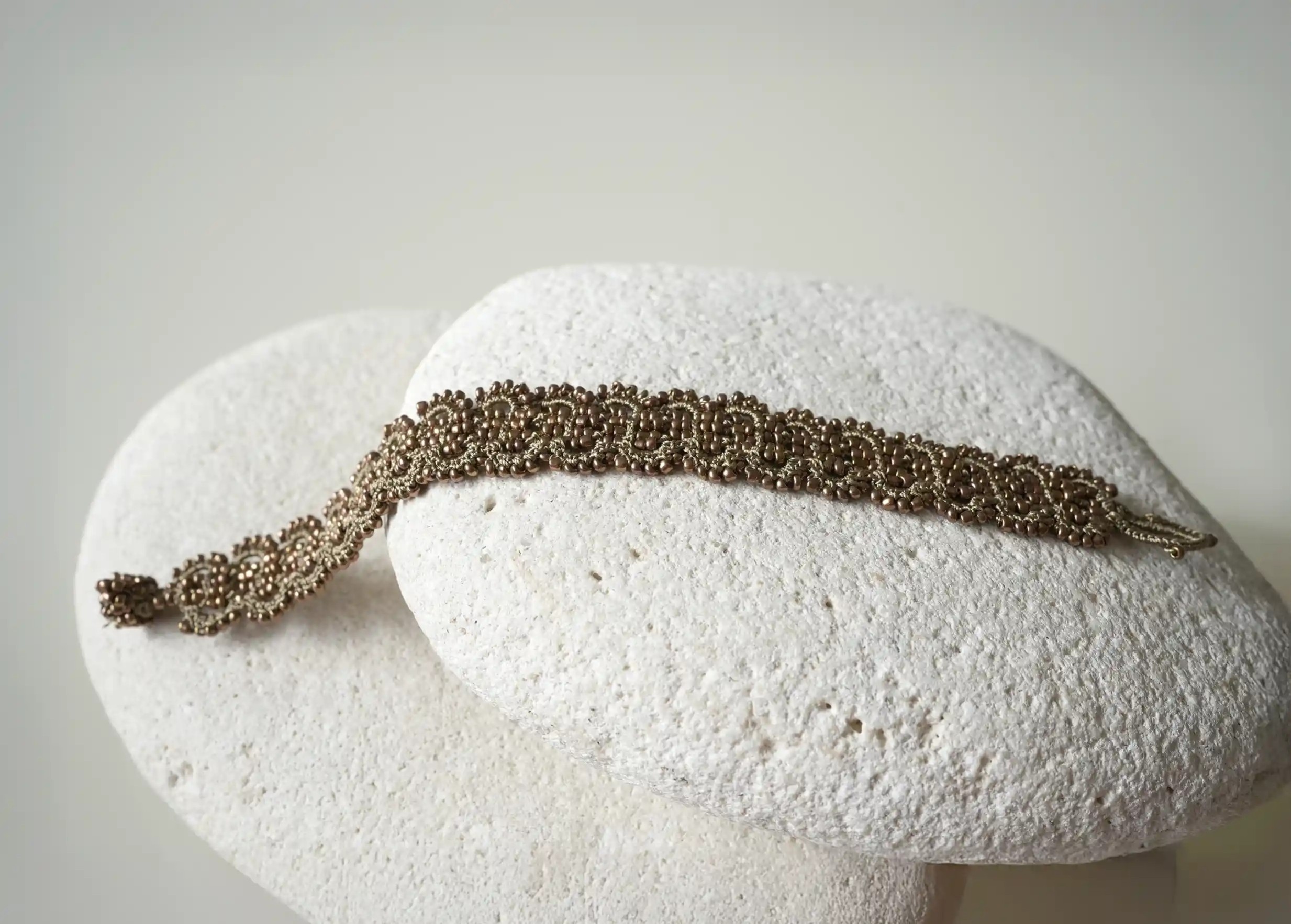 Close-up of the details of the bronze and copper-coloured thread and bead bracelet placed on a pebble, Bark model