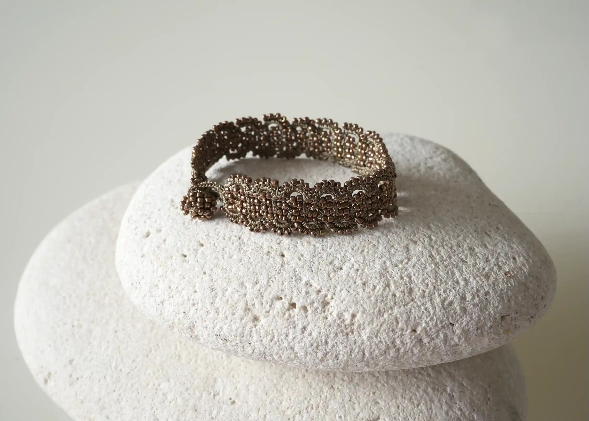 Bracelet made of thread and pearls in glacier blue and silver colours placed on a pebble, Bark model, Karawan brand
