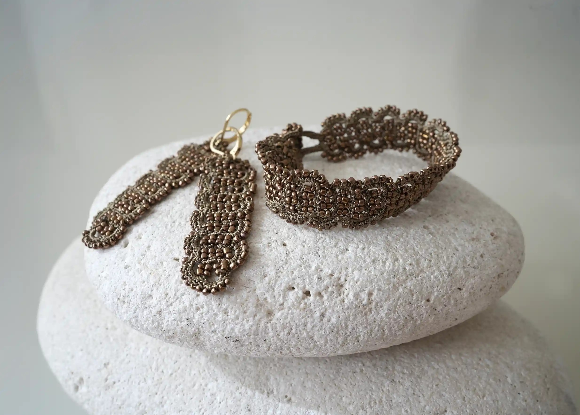 Ensemble de boucle et bracelet en fil et perles coloris bronze et cuivre posés sur un galet, modèle Bark