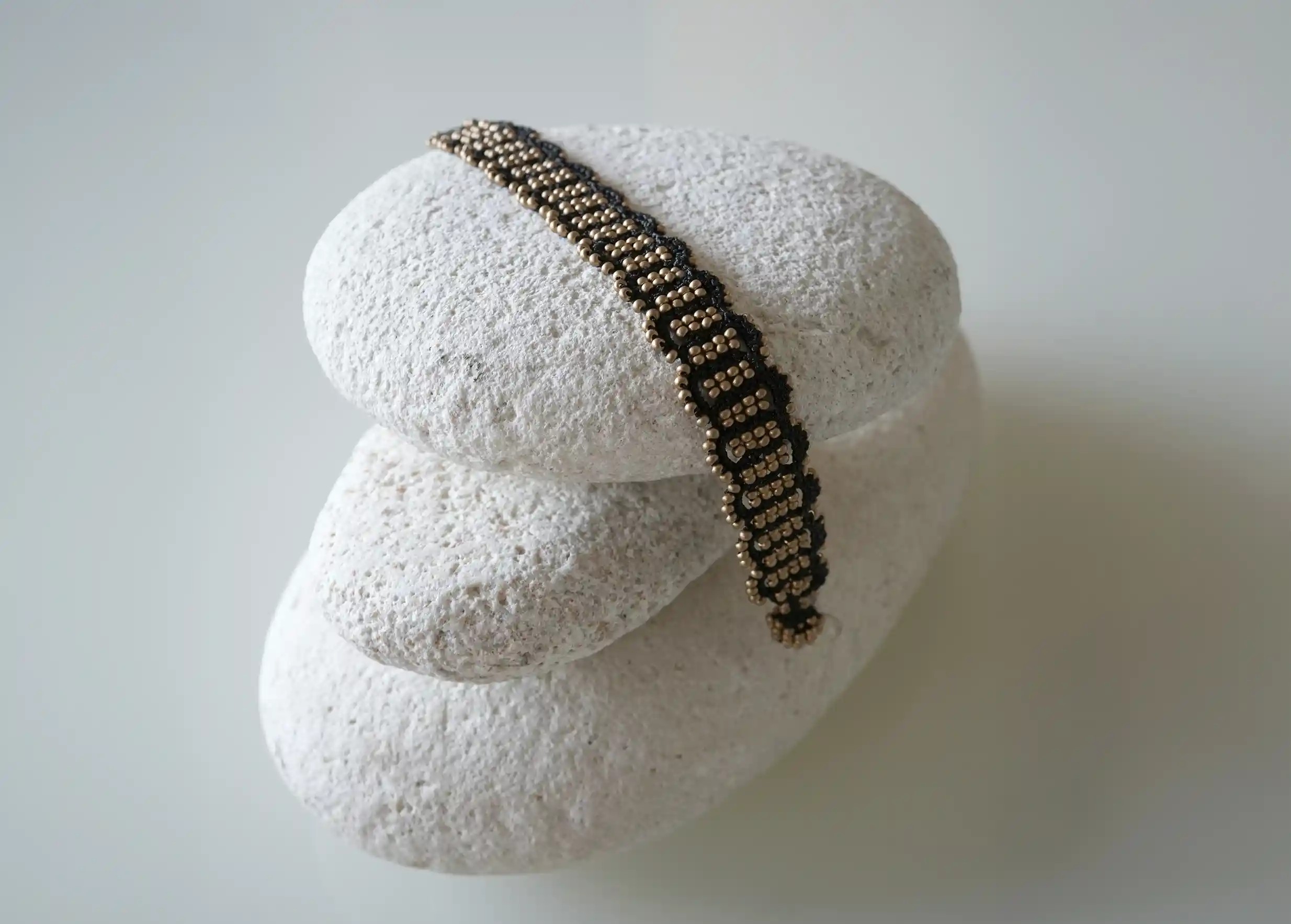 Bracelet en fil et perles coloris noir et or mat posé sur un galet, modèle Bark