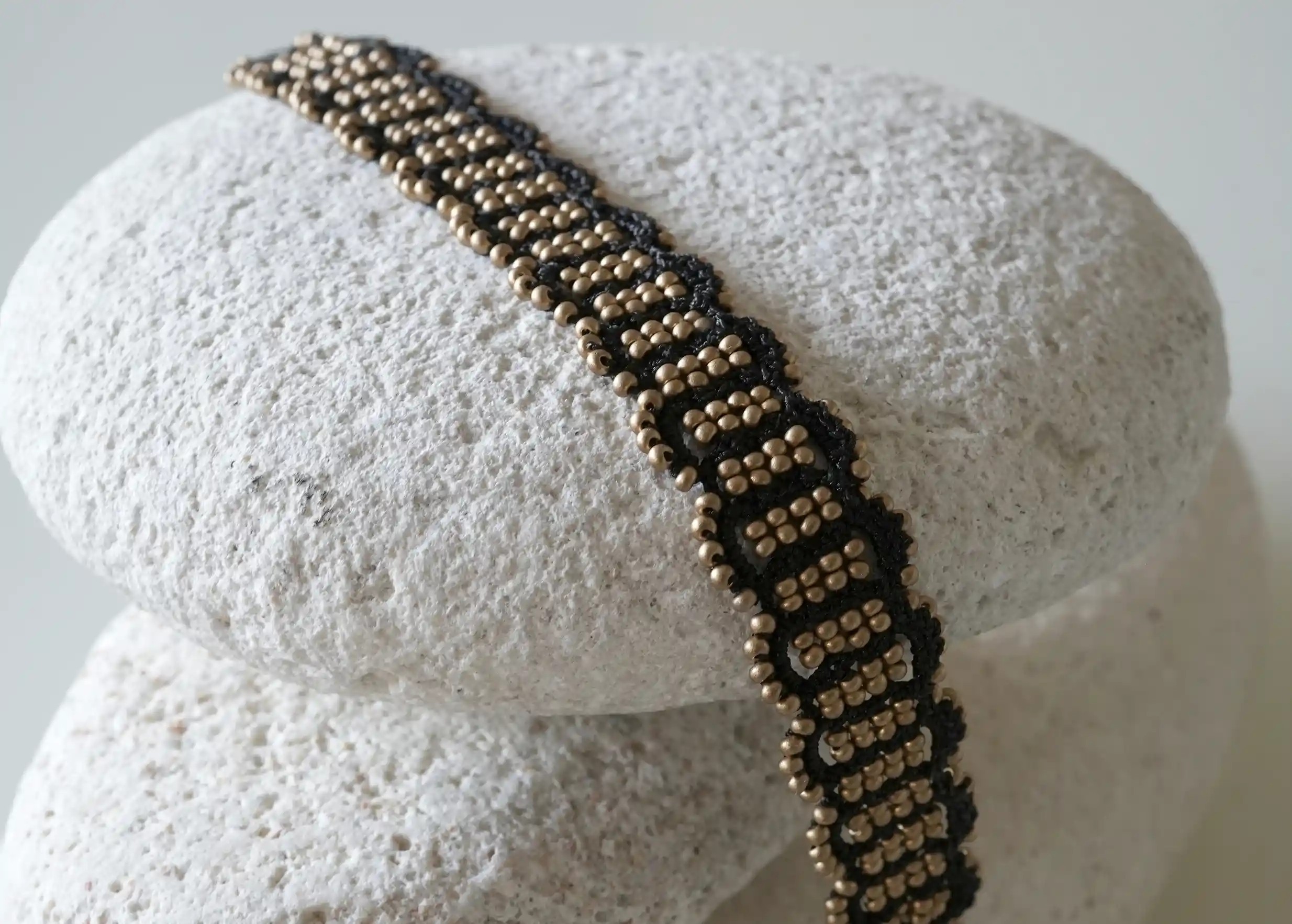 Close-up of the details of the black and matt gold thread and pearl bracelet set on a pebble, Bark model