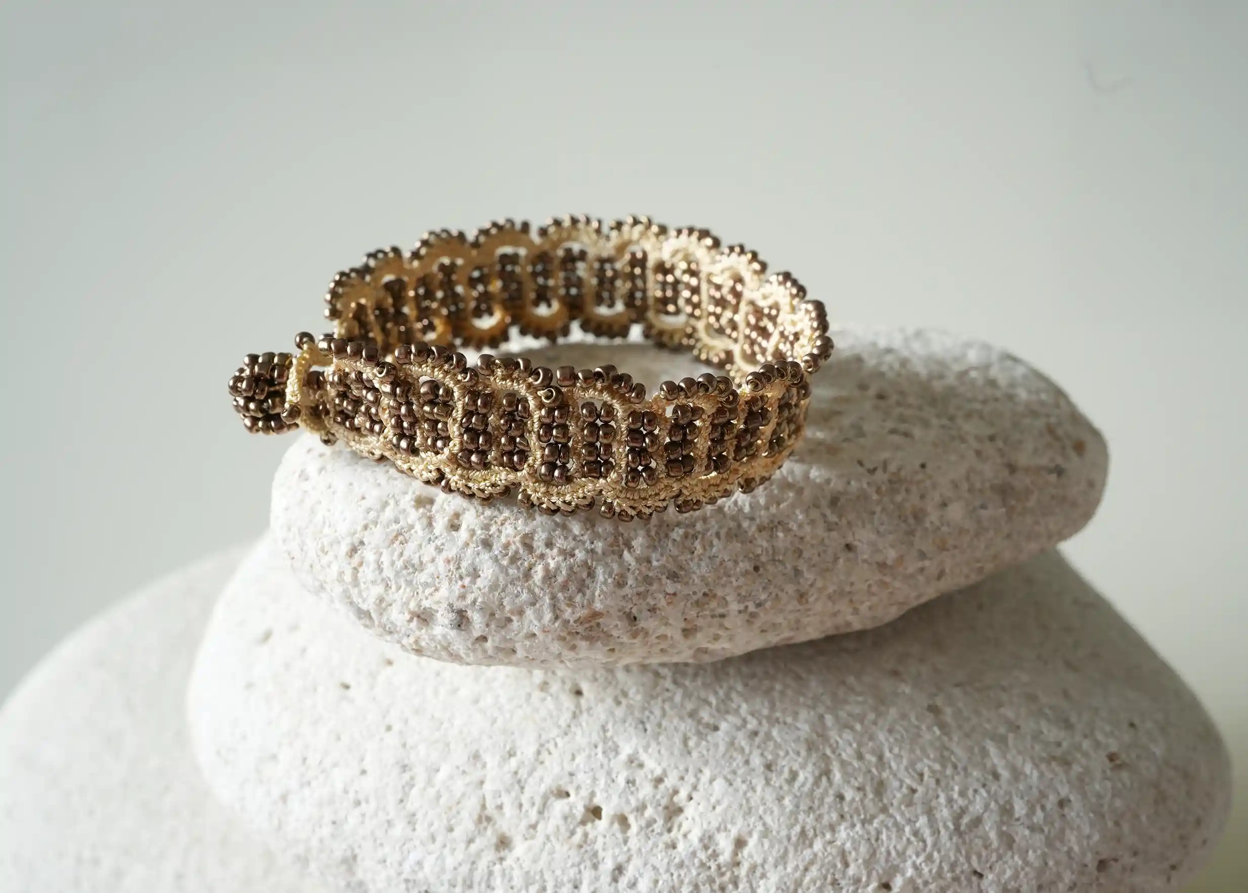 Bracelet en fil et perles coloris or et cuivre et or posé sur un galet, modèle Bark