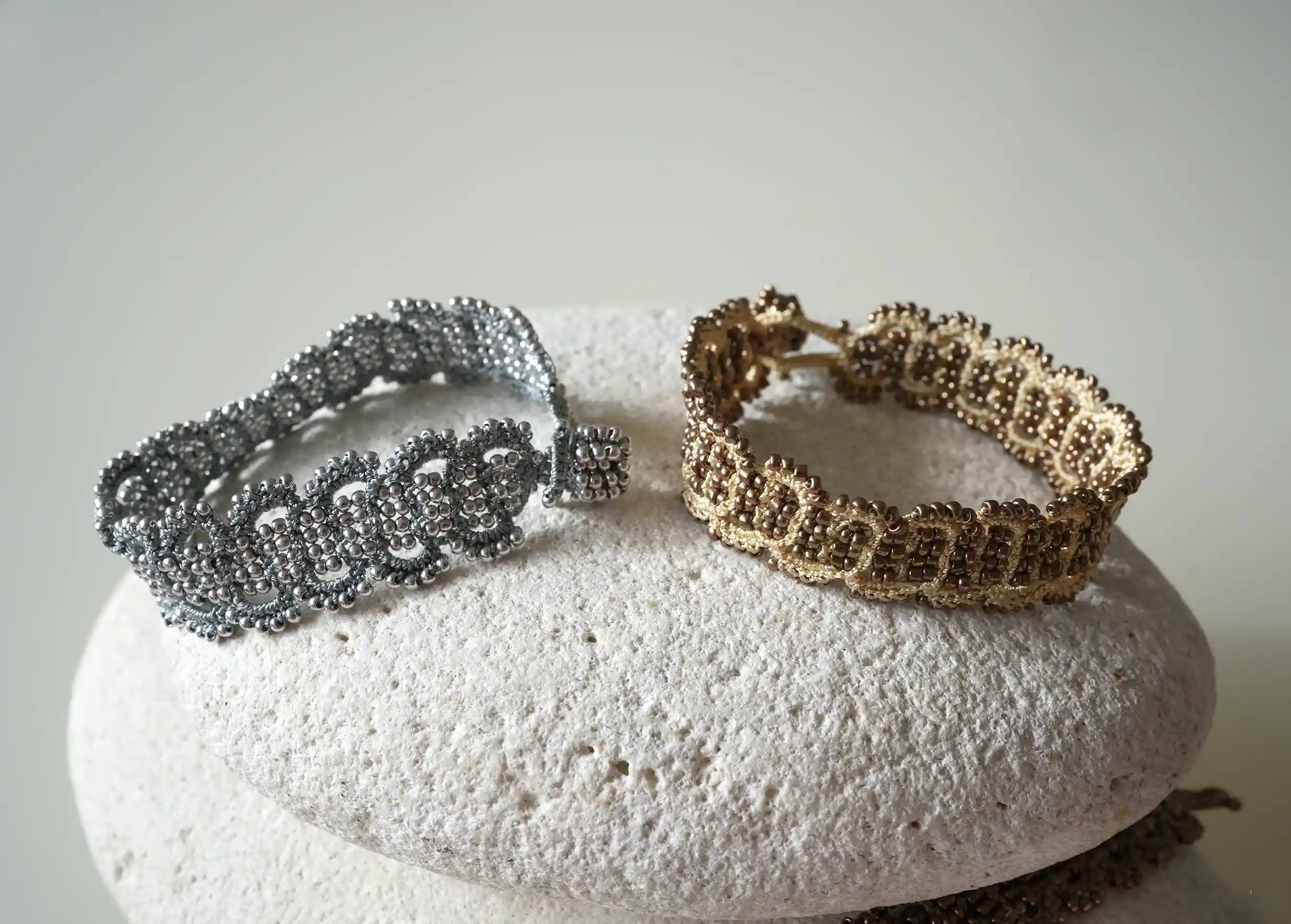 Bracelets made of thread and beads in ivory and gold, grey and silver colours placed on a pebble, Bark models