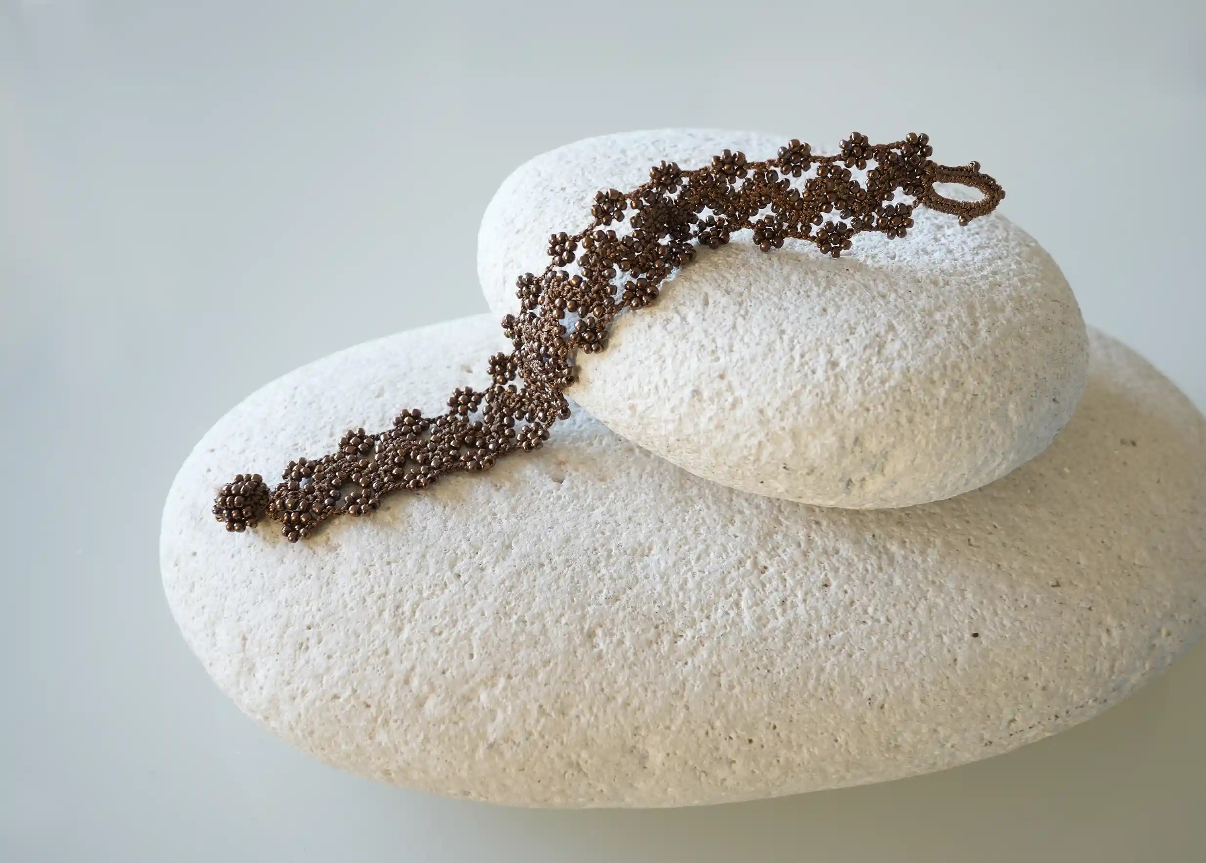 Textile bracelet made of thread and beads, with graphic patterns, Ribbon model in amber brown, placed on a pebble