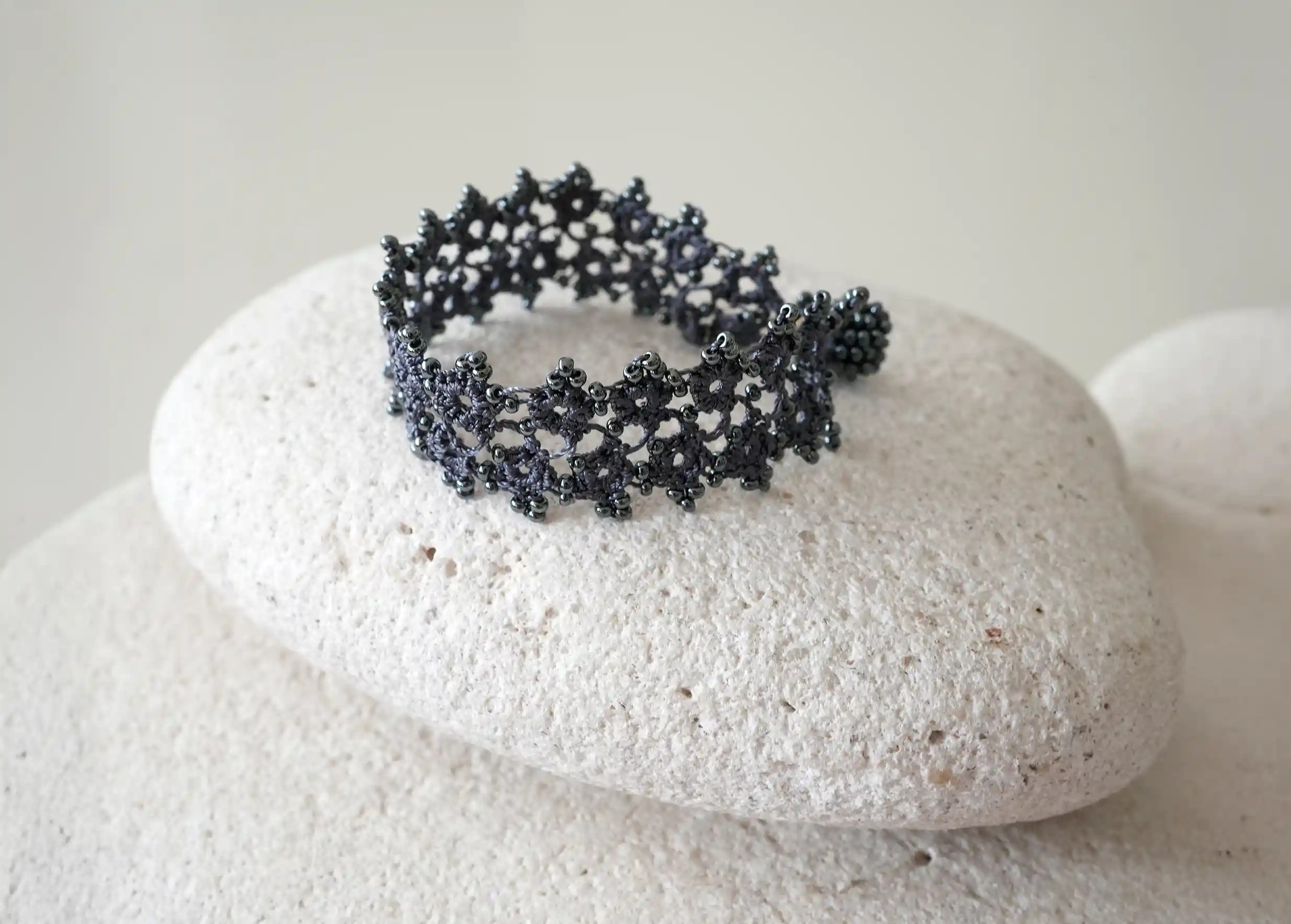 Bracelet textile en dentelle fait main,  Husnu, collection OYA, coloris bleu ardoise posé sur un galet