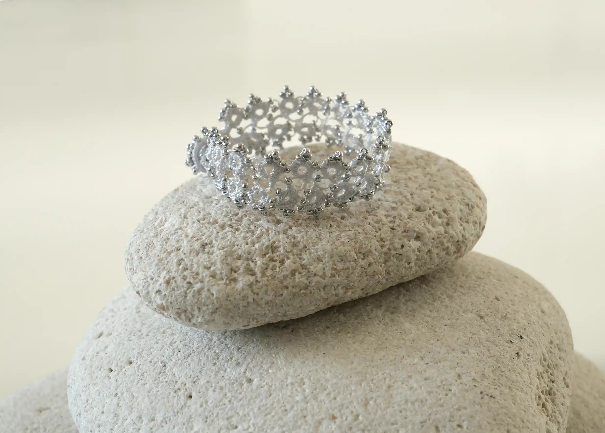 Bracelet textile en dentelle fait main,  Husnu, collection OYA, coloris gris argent posé sur un galet