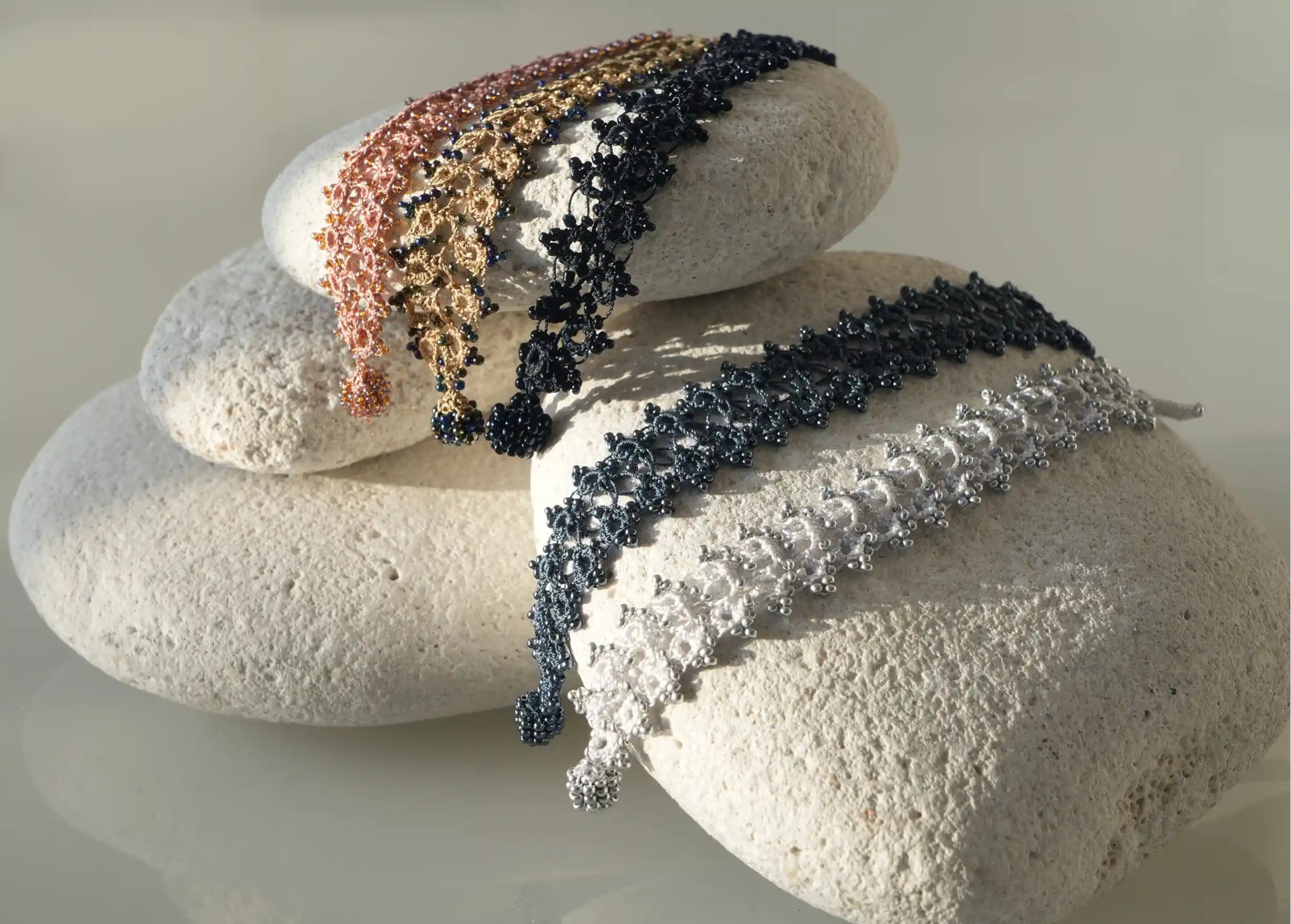 Ensemble de bracelets textiles en dentelle fait main posés sur des galets,  Husnu, collection OYA
